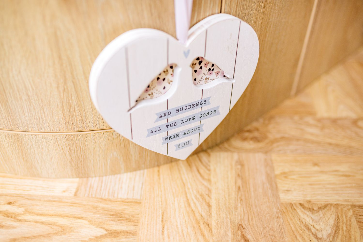 A decorative white wooden heart with delicate text and design hanging against a wooden background.