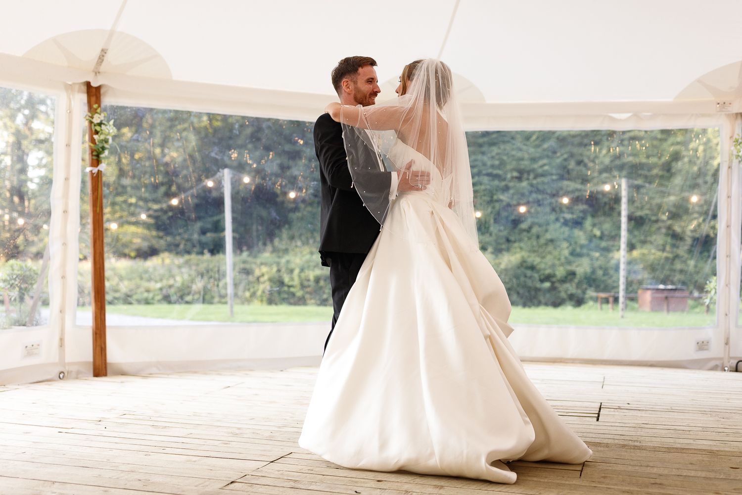 A bride and groom share their first dance under a white tent at an outdoor wedding reception. Gisburne Park Estate