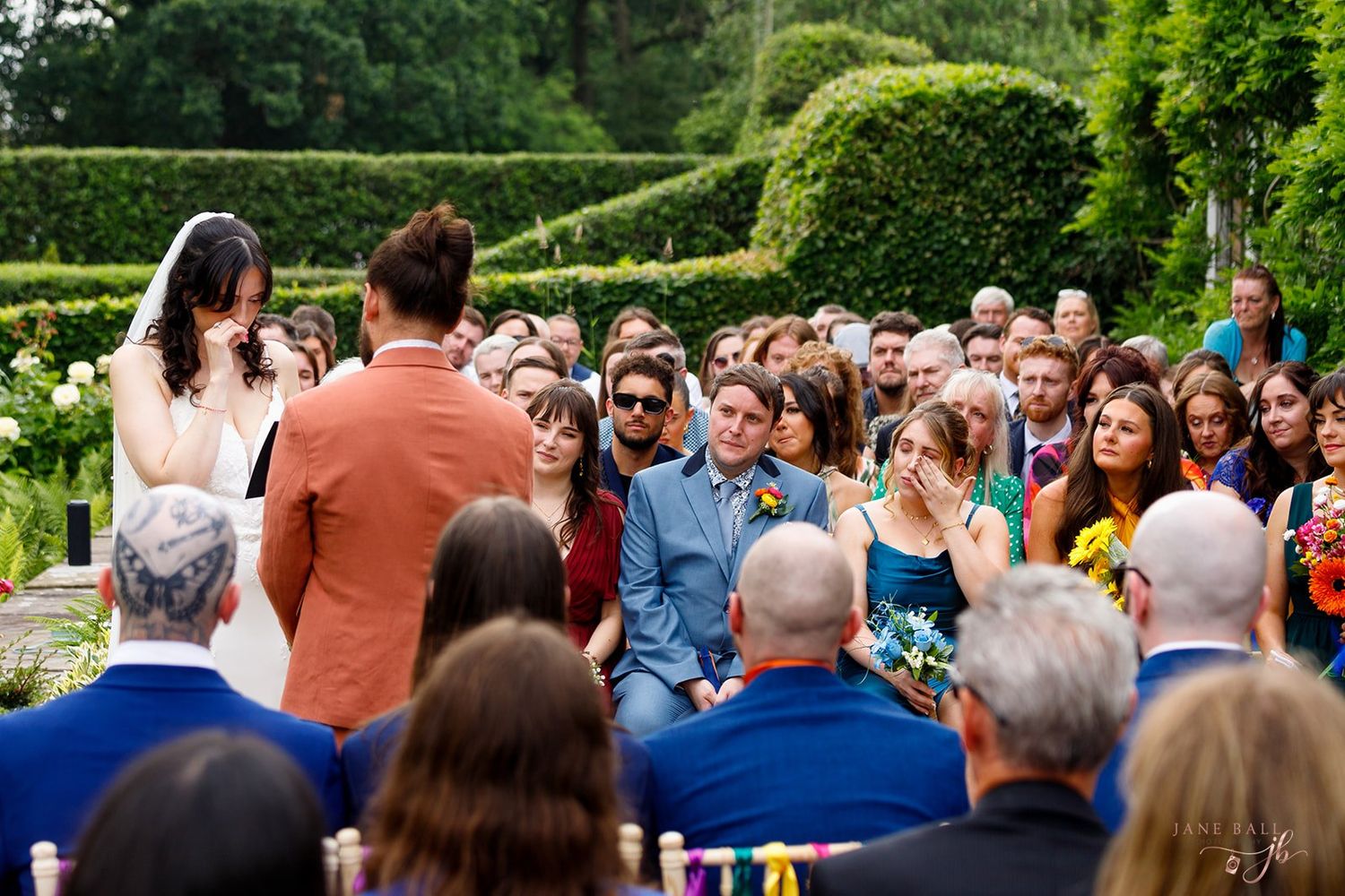 Wedding guests gather outdoors in a garden setting during a summer ceremony.