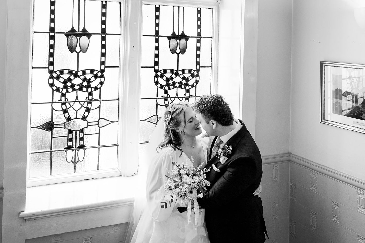 Black and white photo of a bride and groom sharing a kiss in front of stunning stained glass windows.