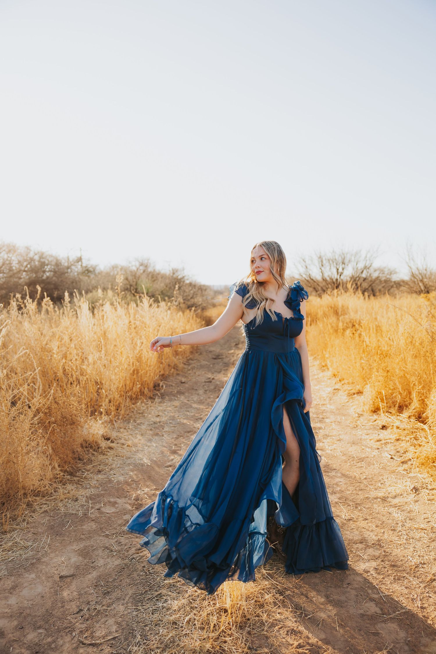 A navy blue tulle dress flows along a golden desert path during sunset.