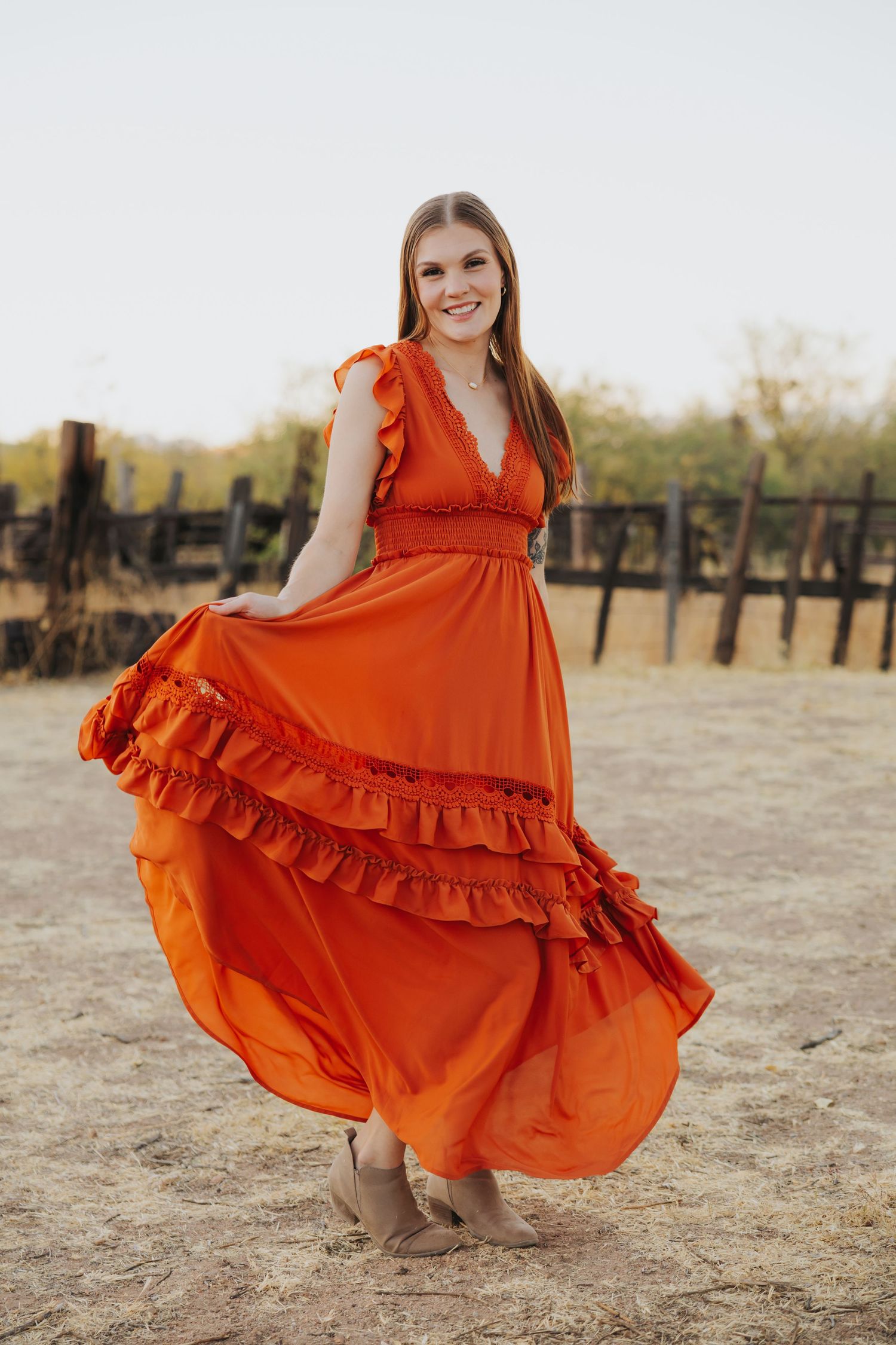 Orange ruffle dress twirling in an outdoor desert setting with wooden fence posts.