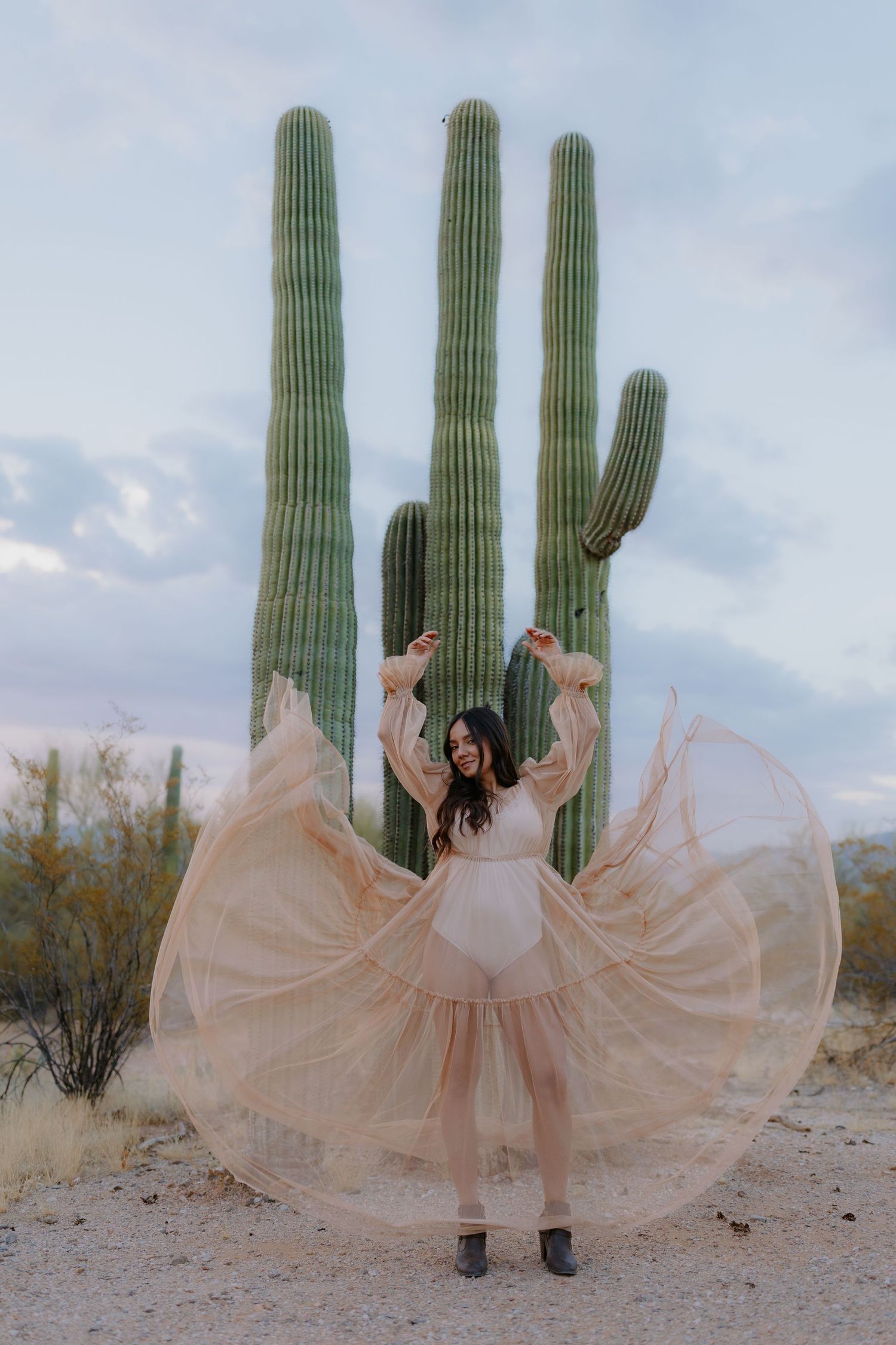 Ethereal peach dresses flowing in the wind against tall saguaro cacti in desert landscape.