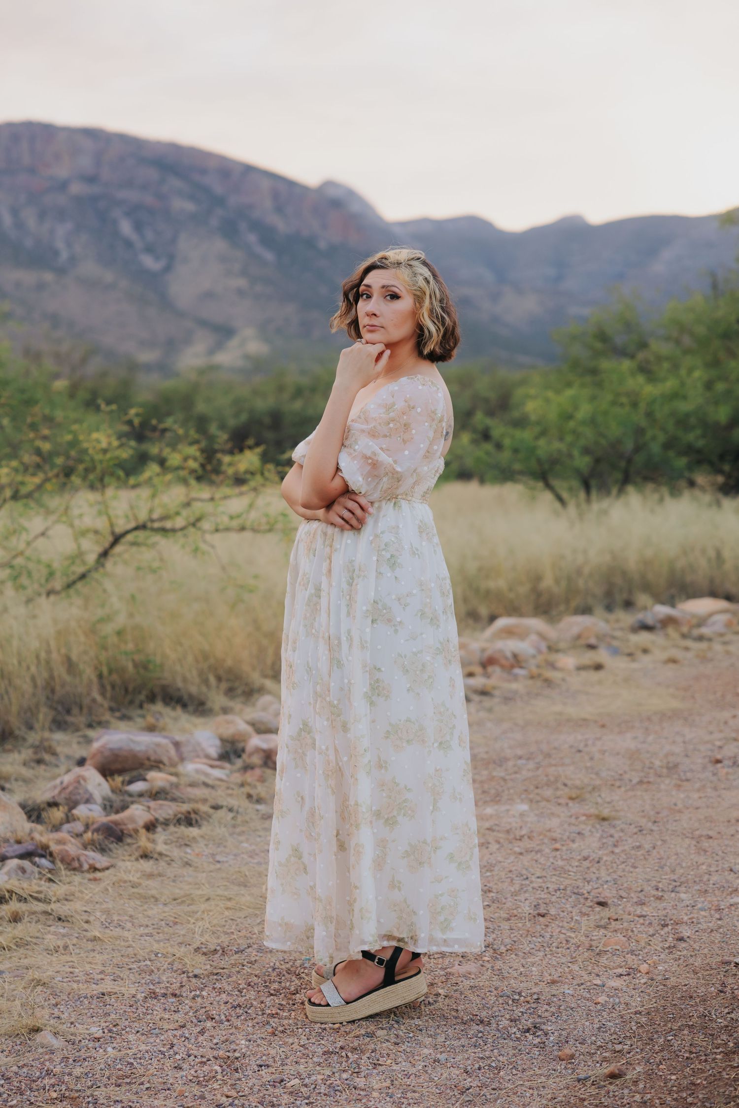 A floral print dress stands out against the desert terrain with mountains in the distance.