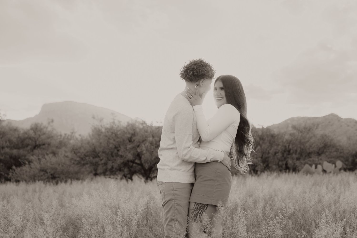 Black and white photo of couple walking together on a desert path with mountains in the distance.