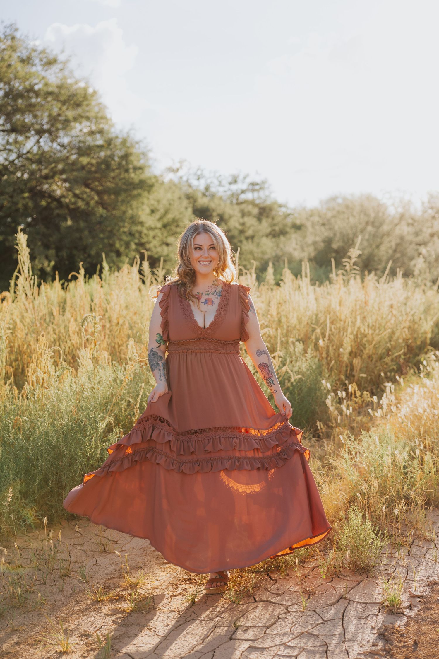 A flowing terracotta dress catches golden light in a natural outdoor setting with tall grass.