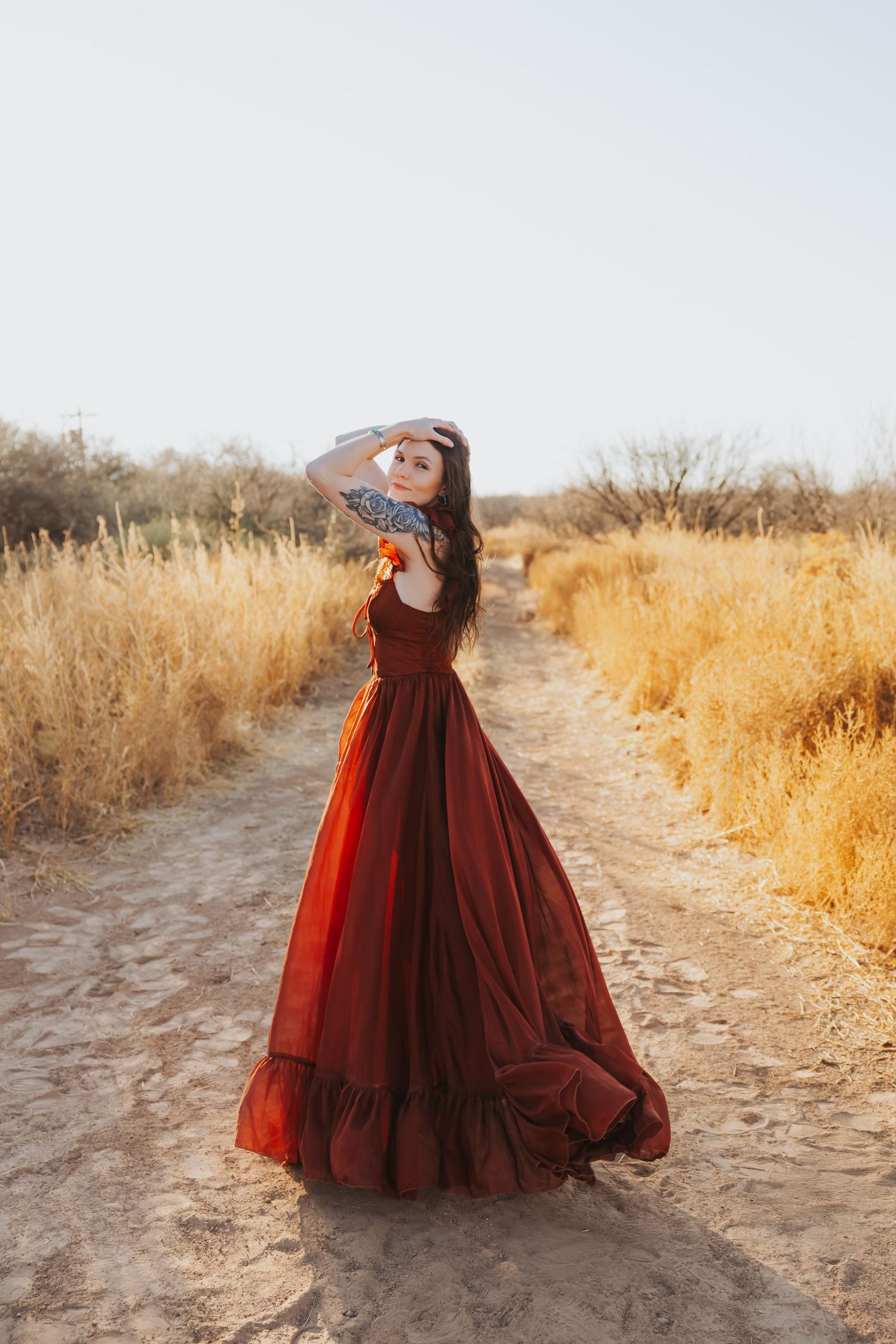 Fashion photography in desert setting with flowing burgundy gown on dirt path.