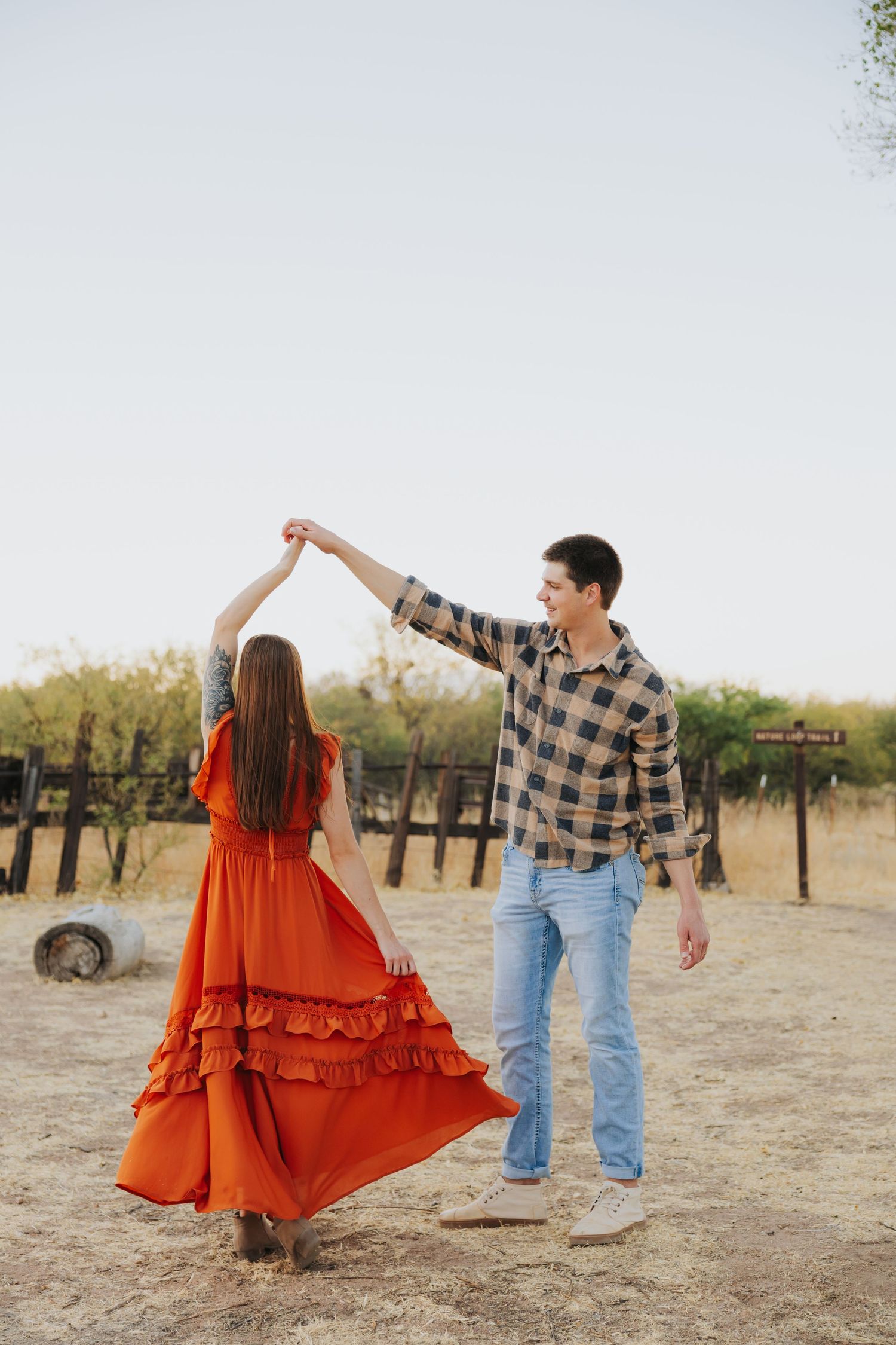 Dancing couple in rustic setting with orange dress flowing in the desert landscape.