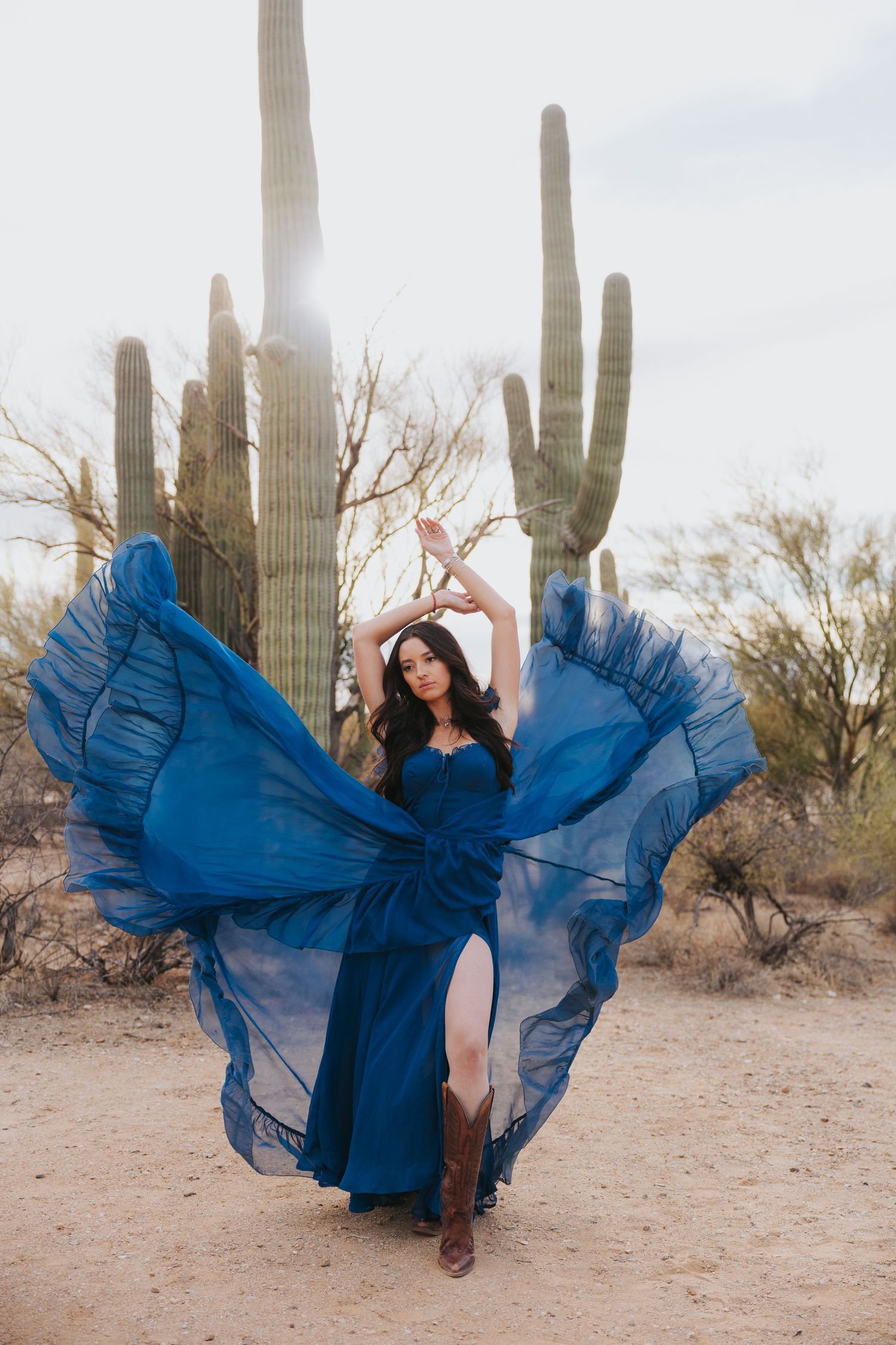 A flowing navy blue dress spins dramatically against a desert backdrop with tall saguaro cacti.