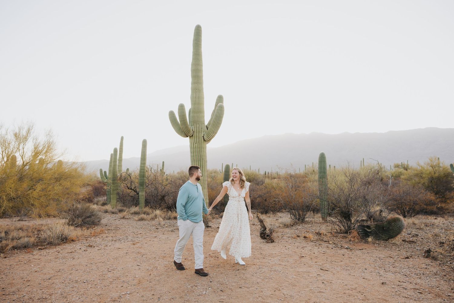 Couple walking through desert landscape surrounded by majestic saguaro cacti at sunset.
