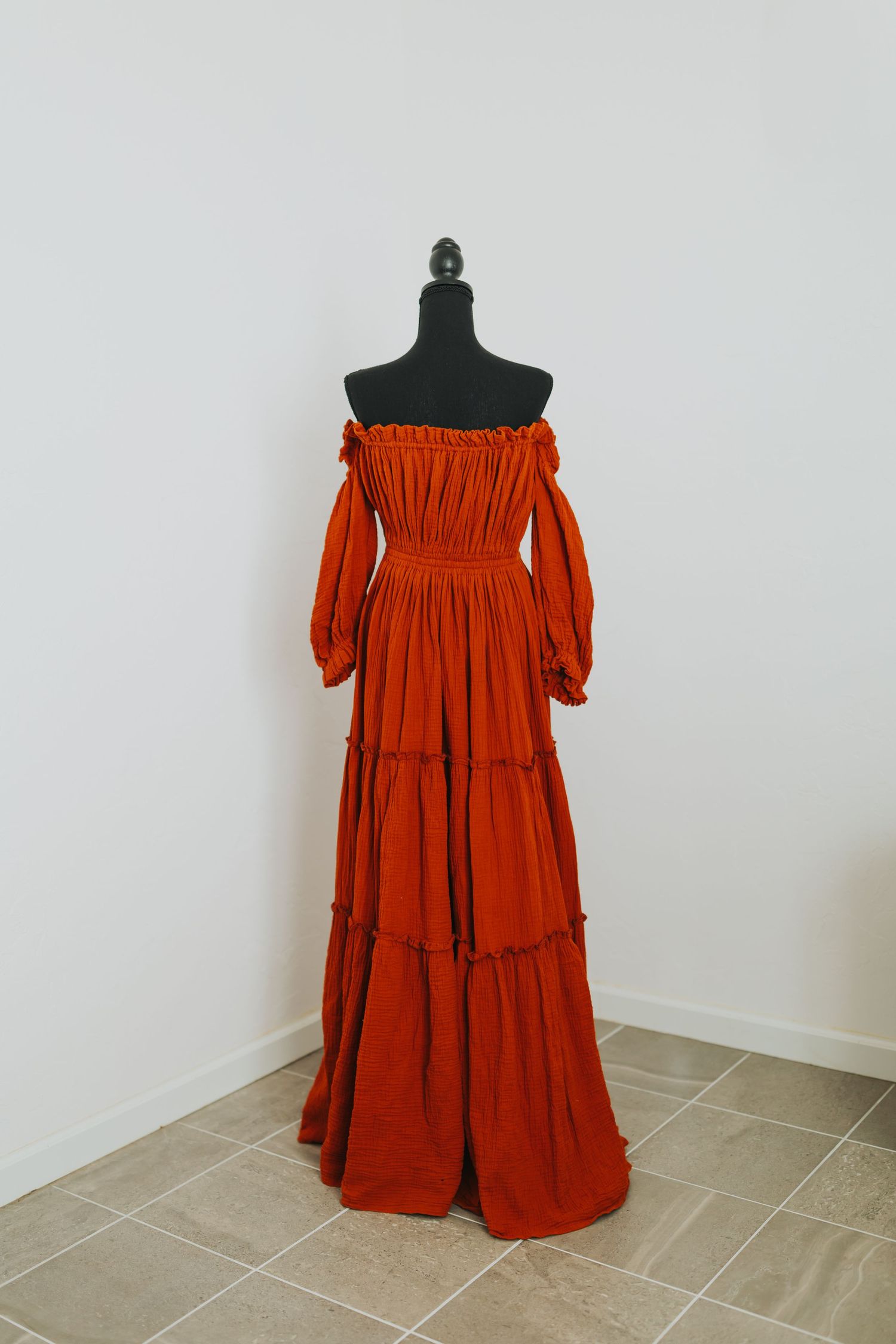 Burnt orange off-shoulder dress with gathered tiers shown on dress form against white background.