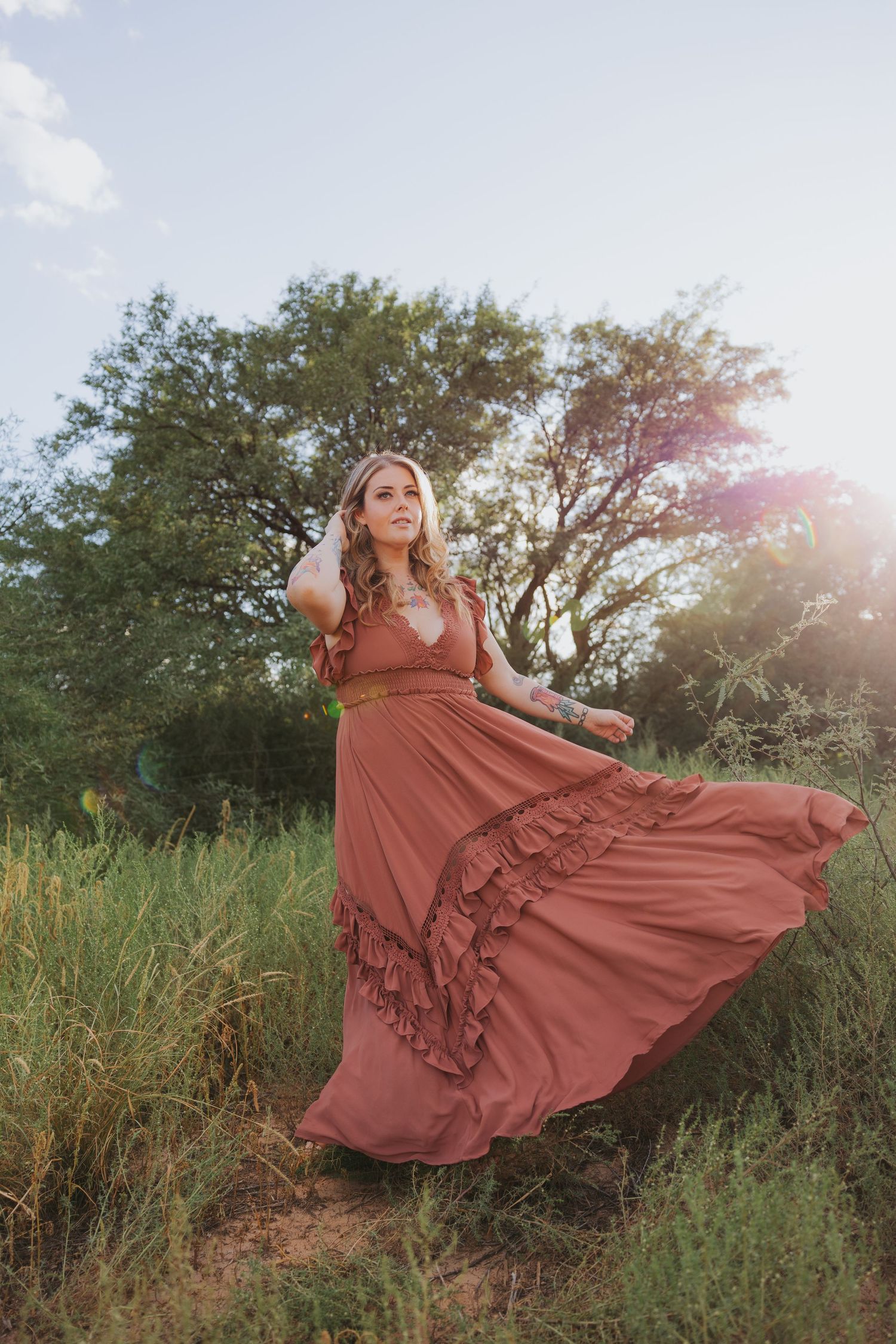 A flowing rust-colored maxi dress with ruffled tiers twirls gracefully in a sunlit meadow setting.
