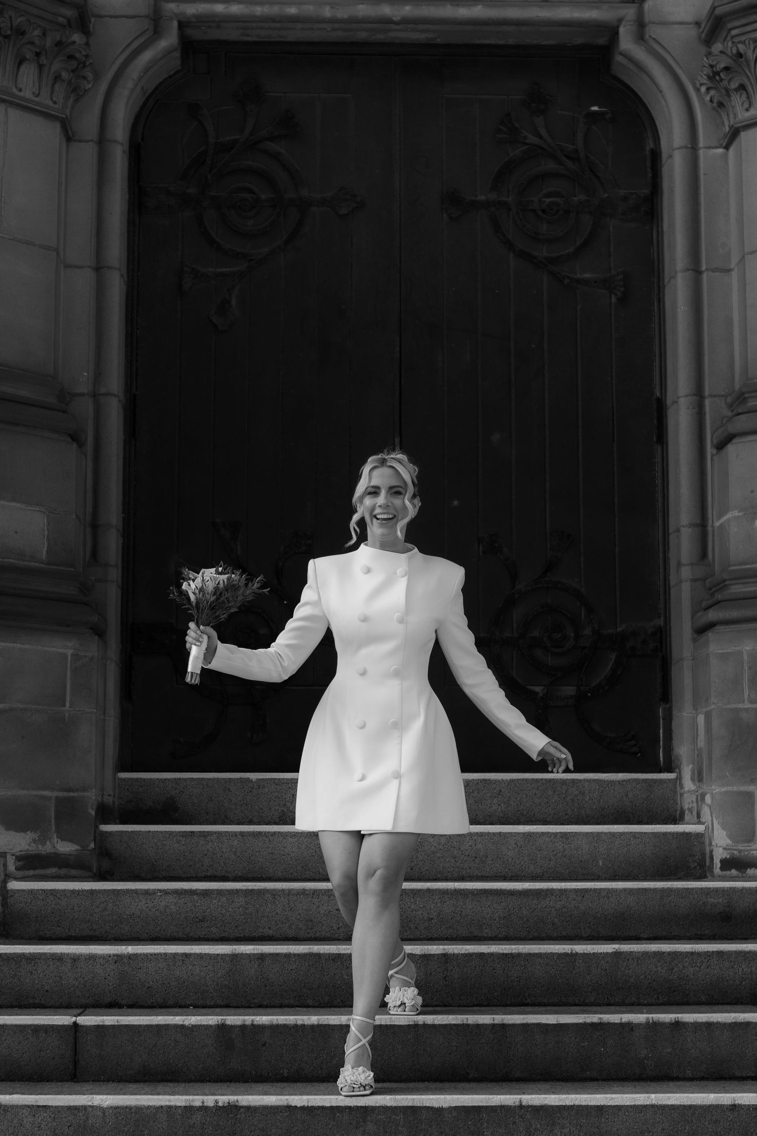 bride walking down stairs at Middlesbrough registry office in odd muse short wedding dress holding bouquet editorial image