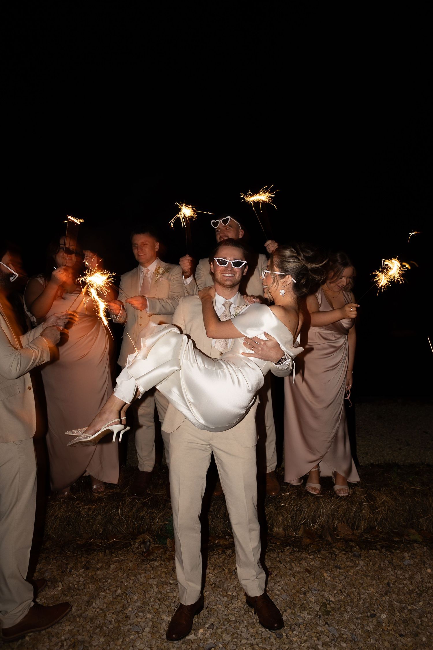groom holding bride in his arms as the bridal party use sparklers around them at Runa Farm wedding Venue based in Barnard castle