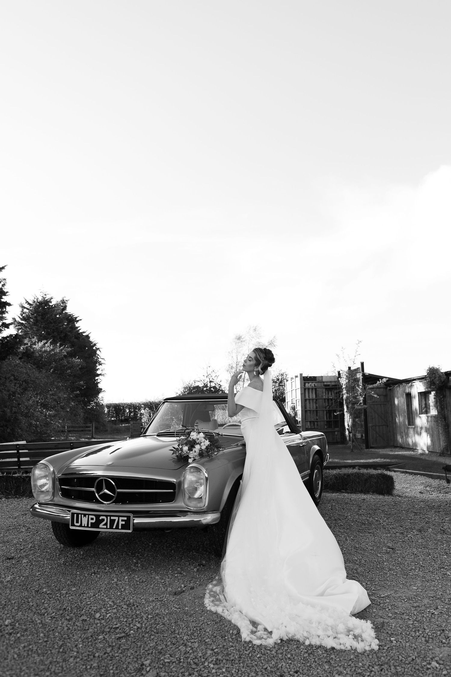black and white image of Bride posing infront of vintage car at wedding venue Runa farm based in Barnard castle