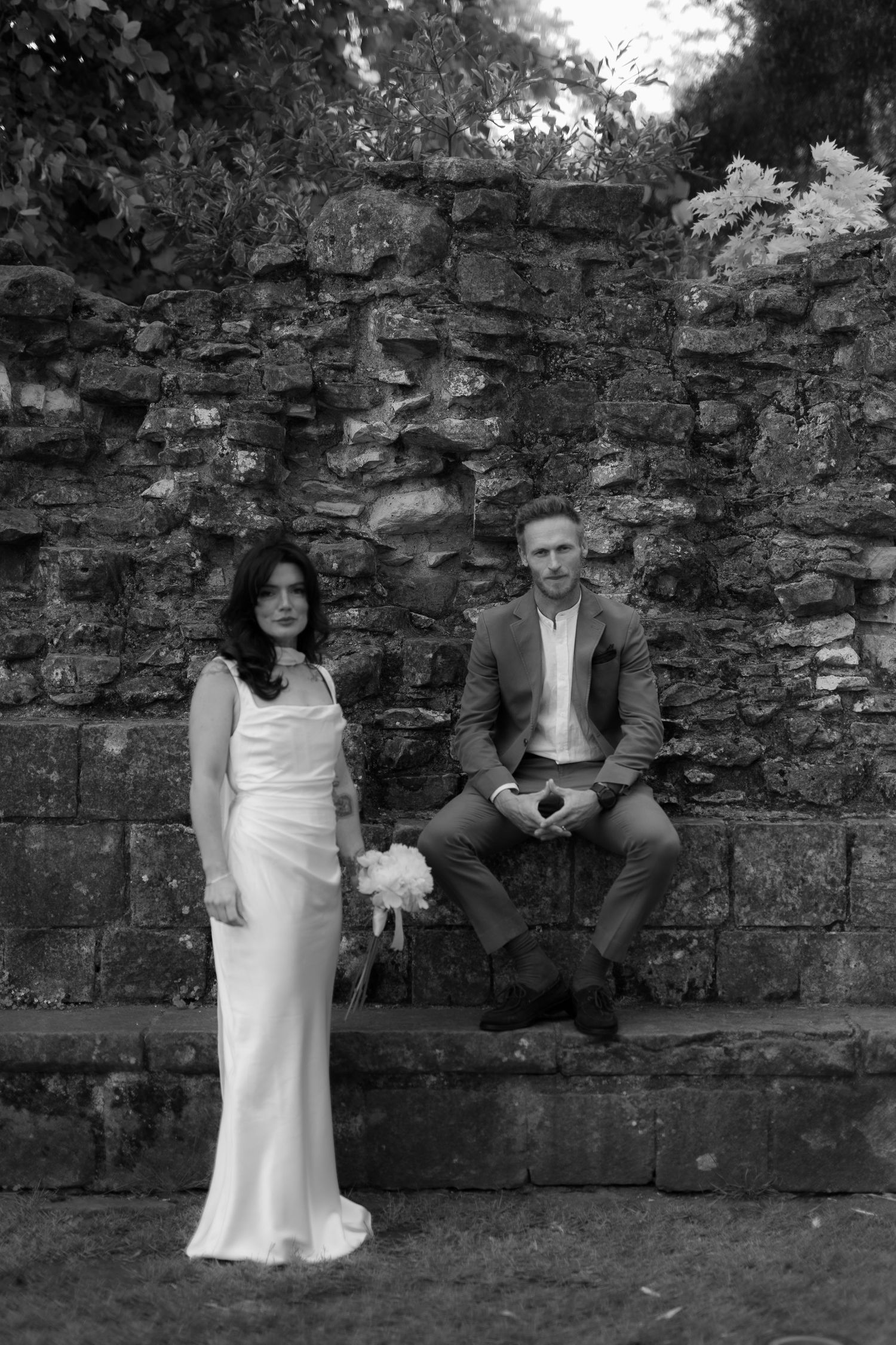 editorial black and white image of groom sitting and bride standing next to him with a serious look in York Museum gardens