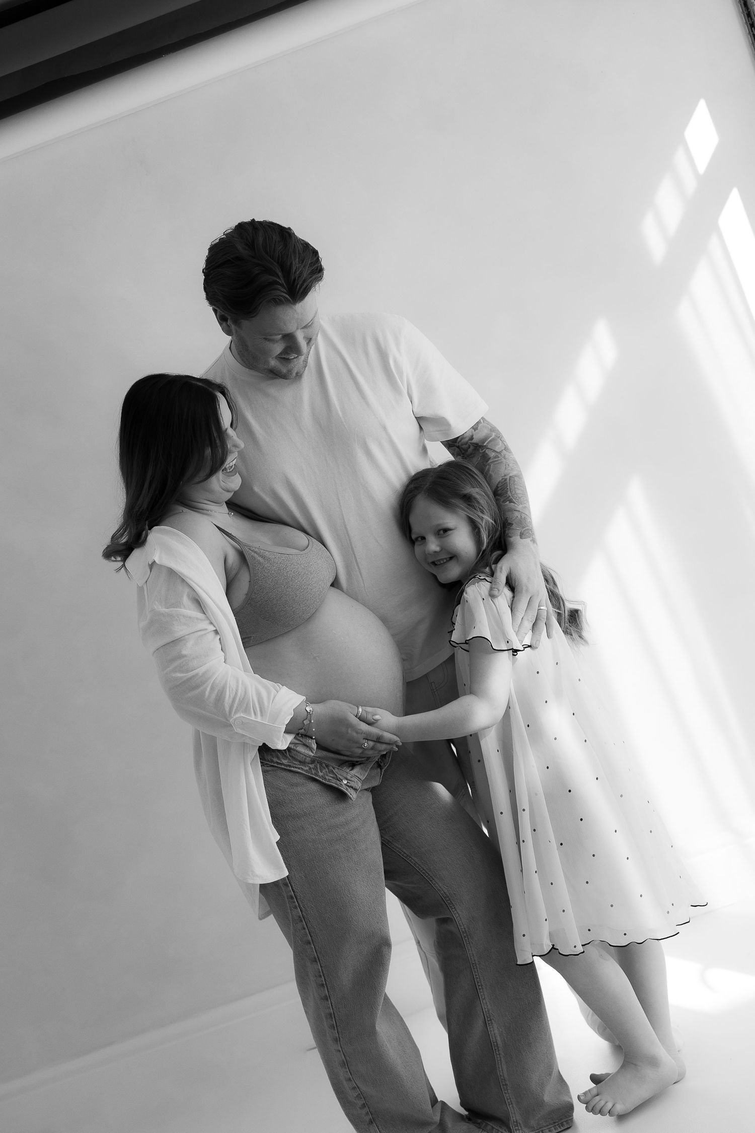 mother , father and daughter cuddling newborn bump showing their bond for each other during their maternity studio session.