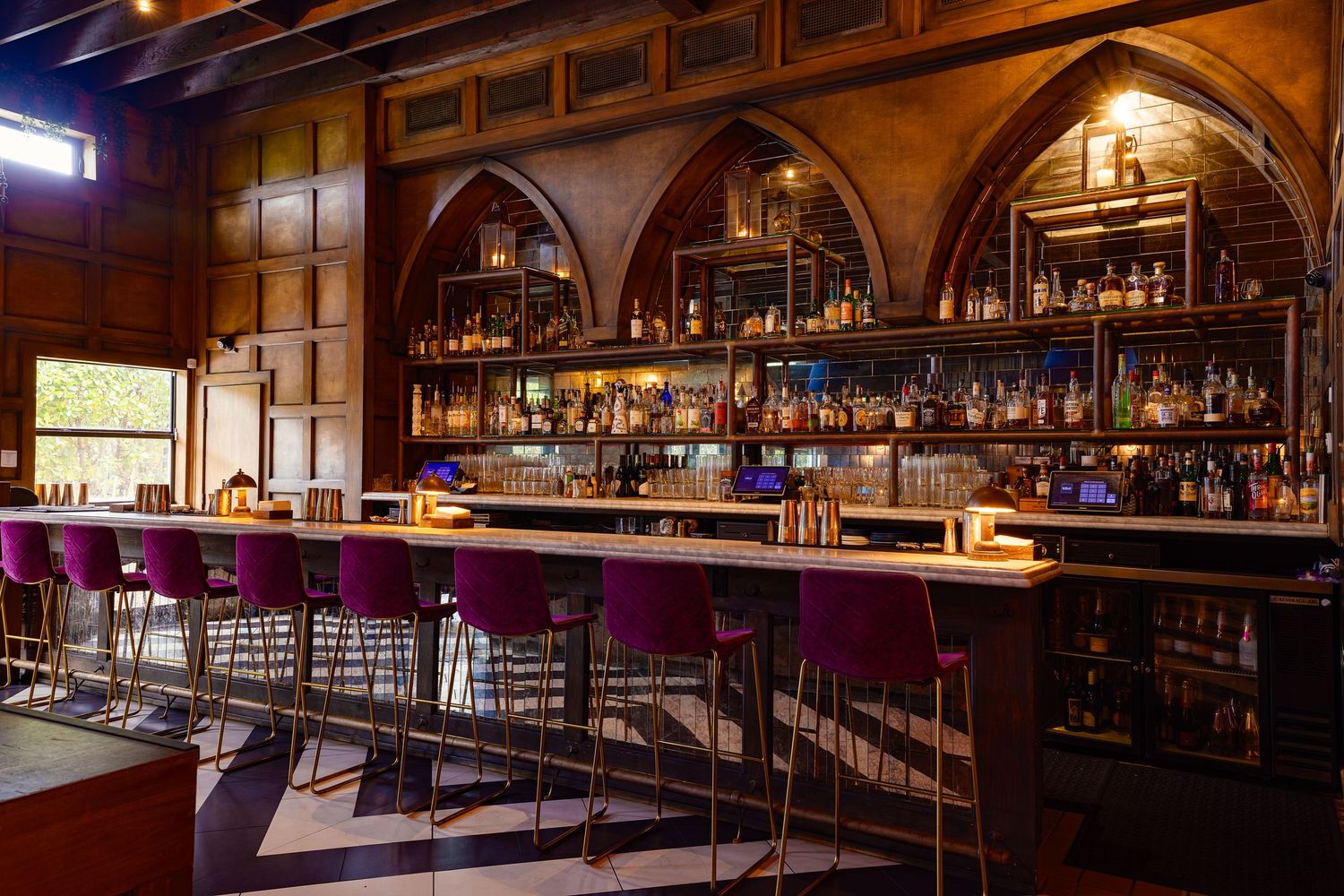 Elegant bar interior with arched shelving, moody lighting, & plush seating—showcasing luxury hospitality design via high-end interior photo