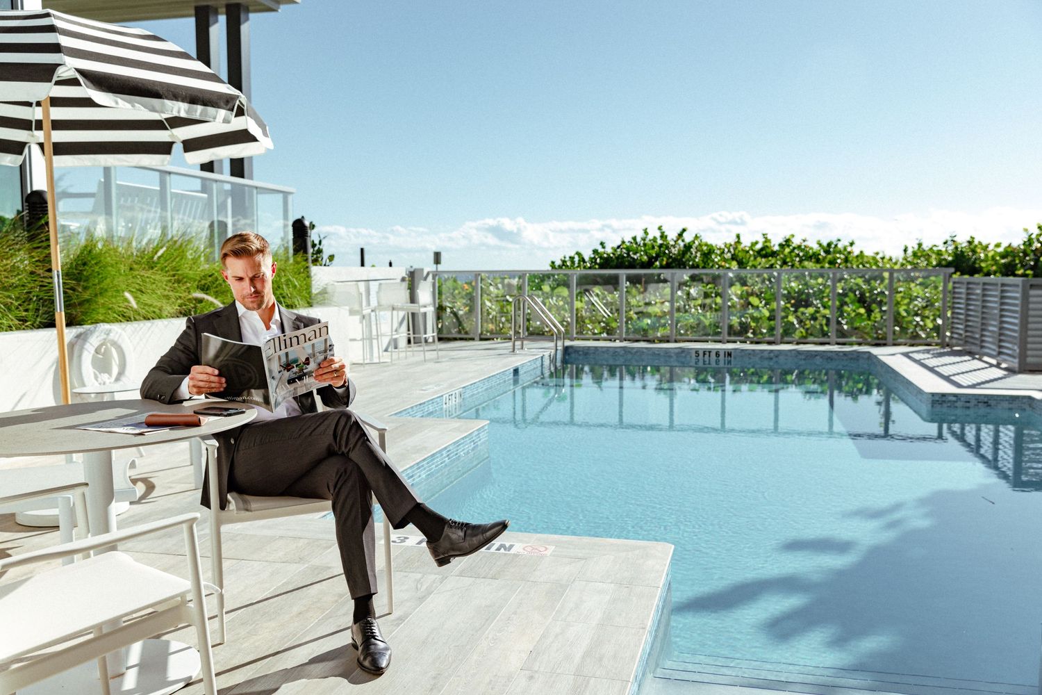Personal branding photography of high end luxury realtor in suit reading newspaper at luxury poolside location in South Florida.