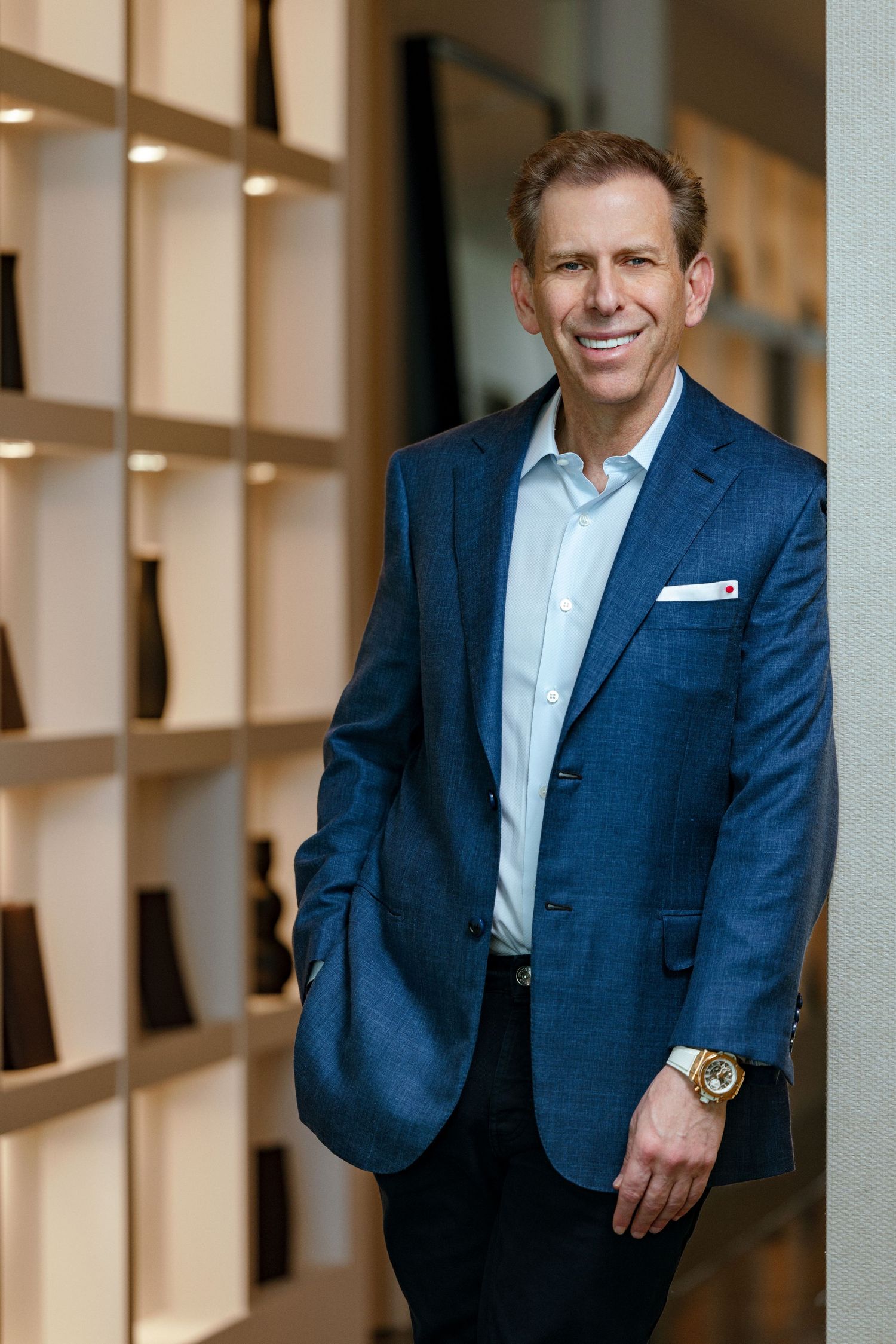 Personal branding portrait of Michael Liebowitz, CEO of Douglas Elliman, standing confidently in a blue suit in modern office interior.