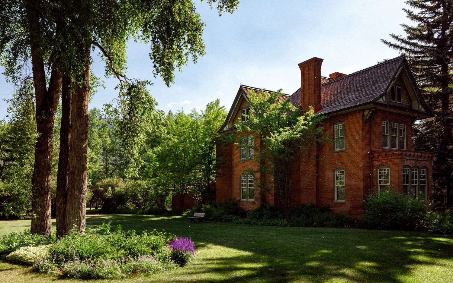 Architectural photography of historic red brick house with gabled roof, large windows, and manicured landscaping in wooded setting.