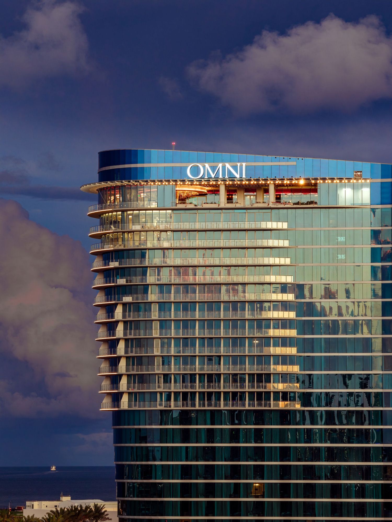 Architectural photography of the Omni Hotel high-rise at dusk, featuring curved glass façade, illuminated rooftop, and modern urban design.