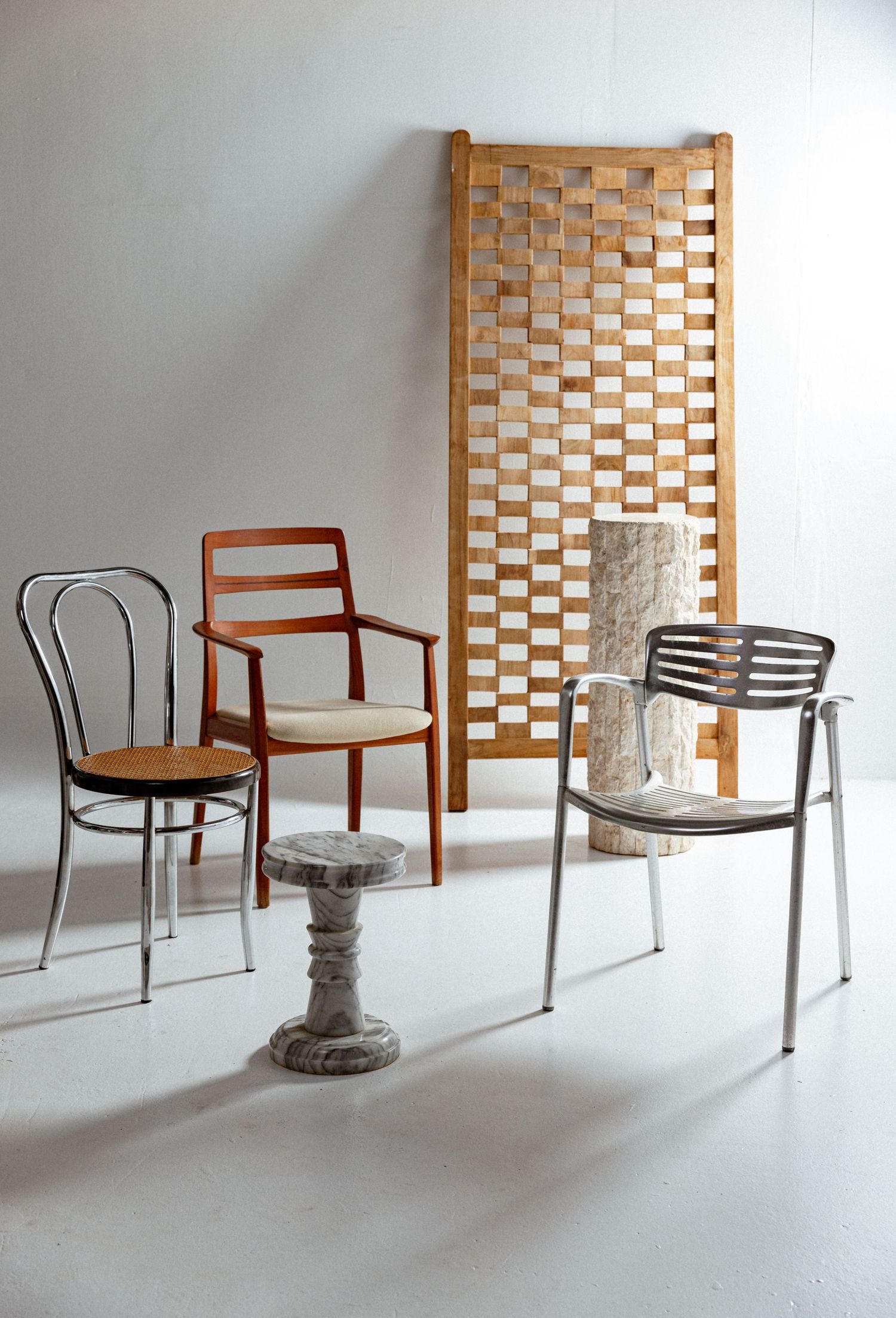 Product photography of vintage metal and wood chairs styled with a woven room divider in a minimalist studio setting.
