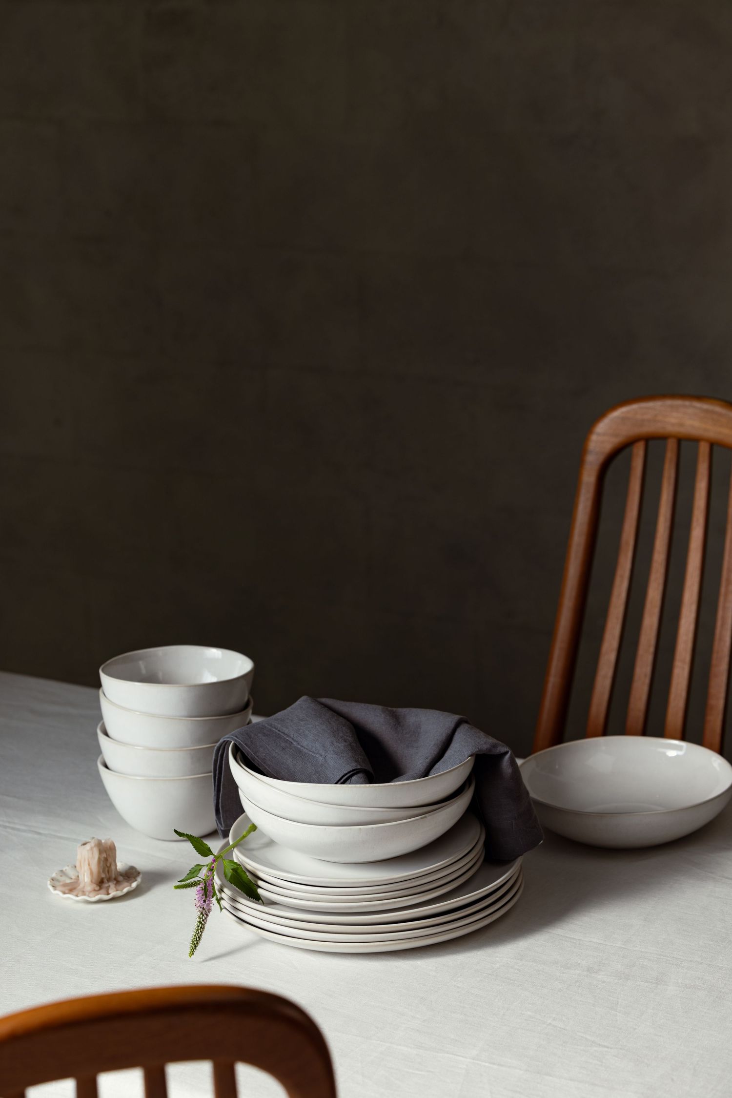 Product photography of handcrafted ceramic plates and bowls stacked on a linen table, showcasing minimalist design and neutral tones.