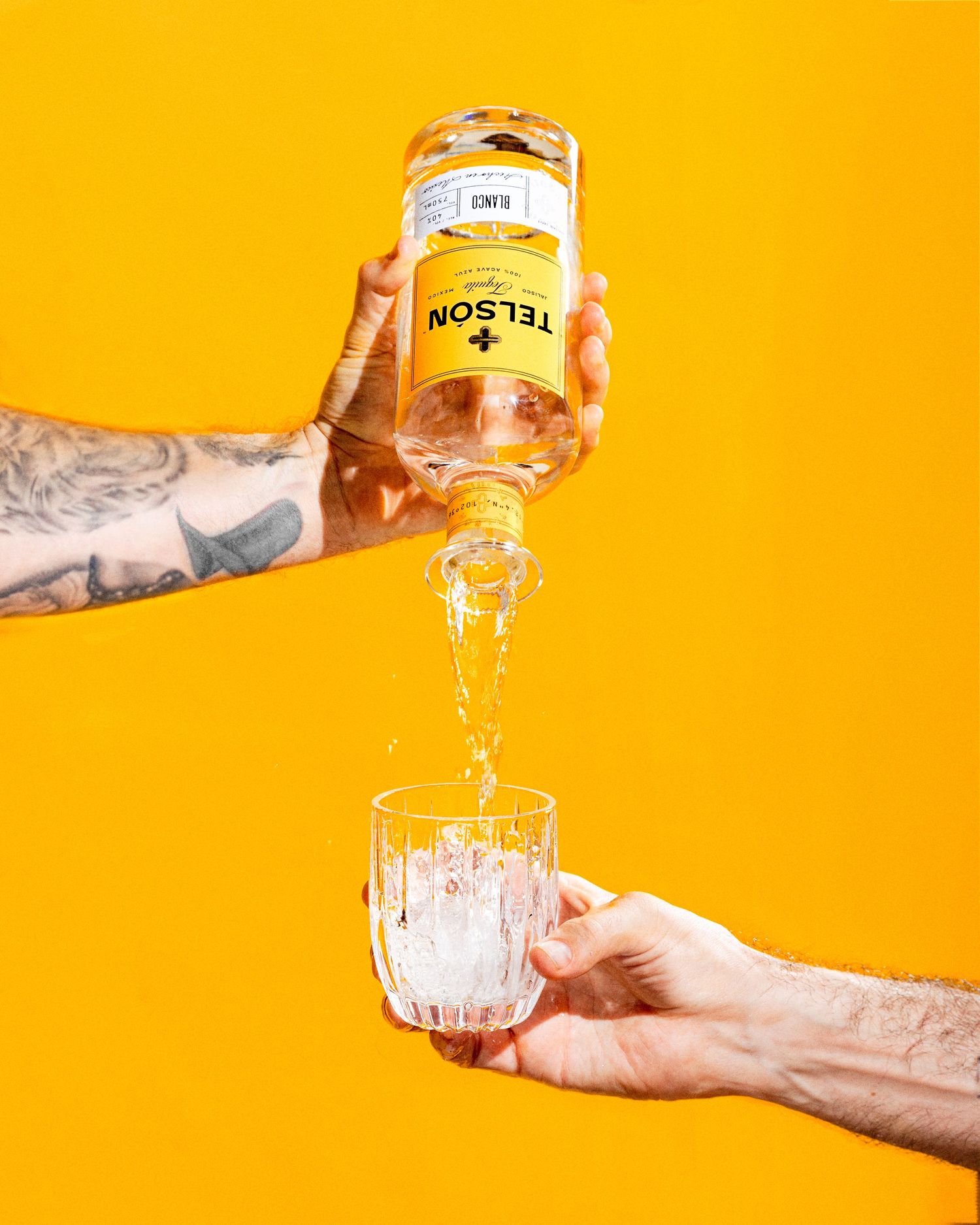 Creative beverage photography of Telsón tequila being poured into a glass with vibrant yellow backdrop.