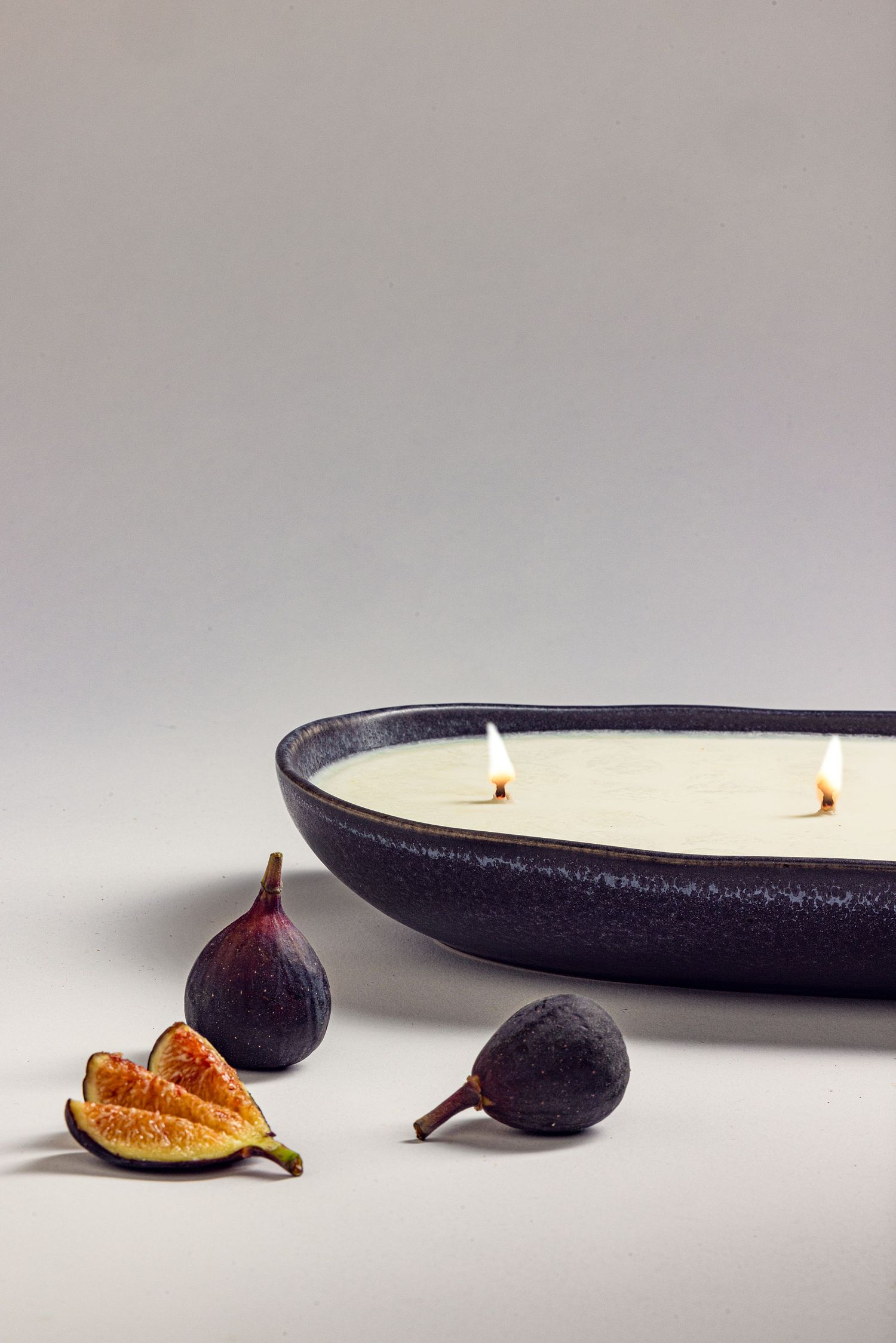 Product photography of a ceramic candle styled with fresh figs on a neutral backdrop, highlighting handcrafted design.