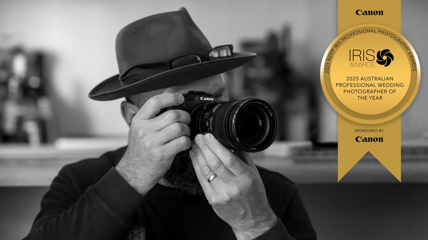 A black and white Image of Jason Robins wearing his Akubra Hat, a Professional photographer taking a photo with a Canon DSLR camera.