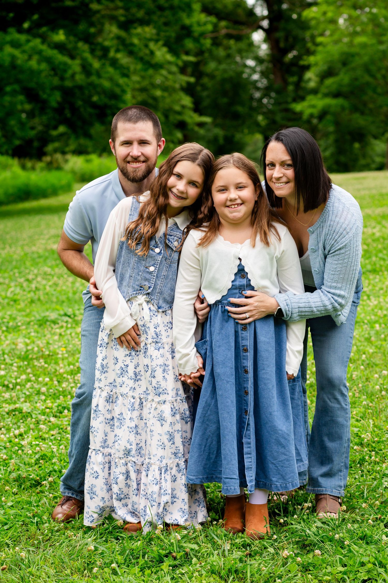 Family of four with two girls in denim skirts posing together on a lush green lawn.