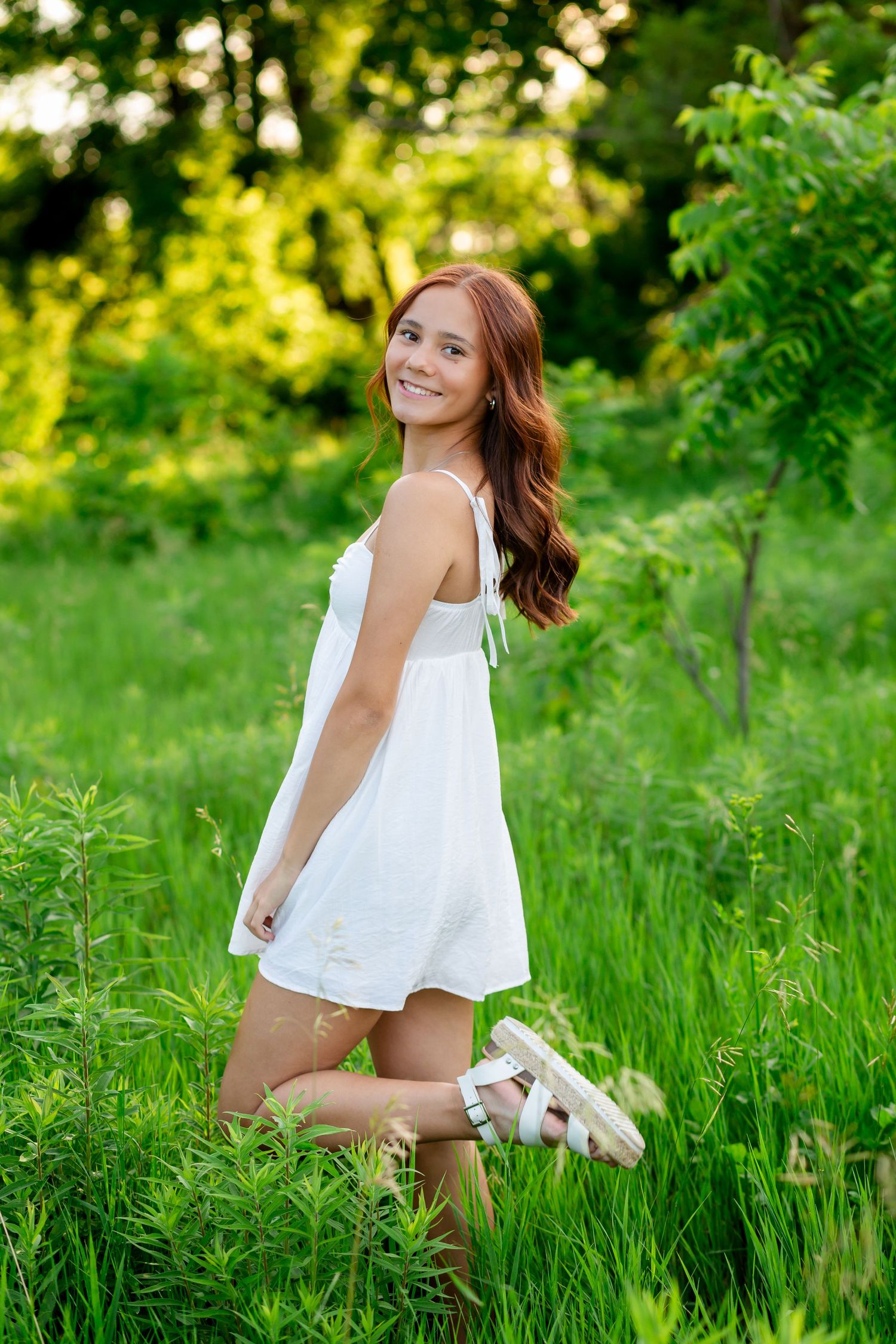 Smiling young woman in white sundress standing in lush green garden.