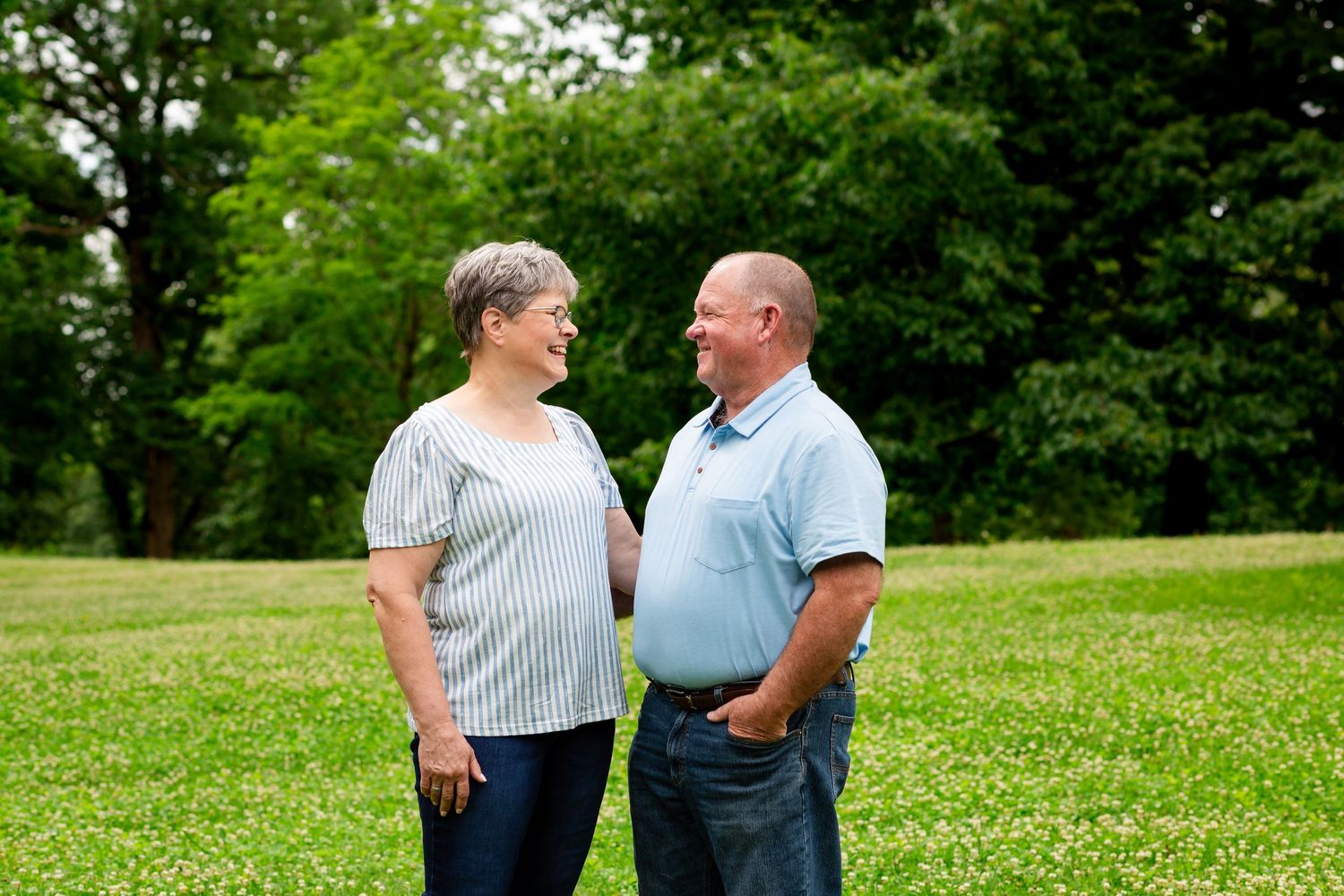 Couple standing face to face smiling in a lush green park on a sunny day.
