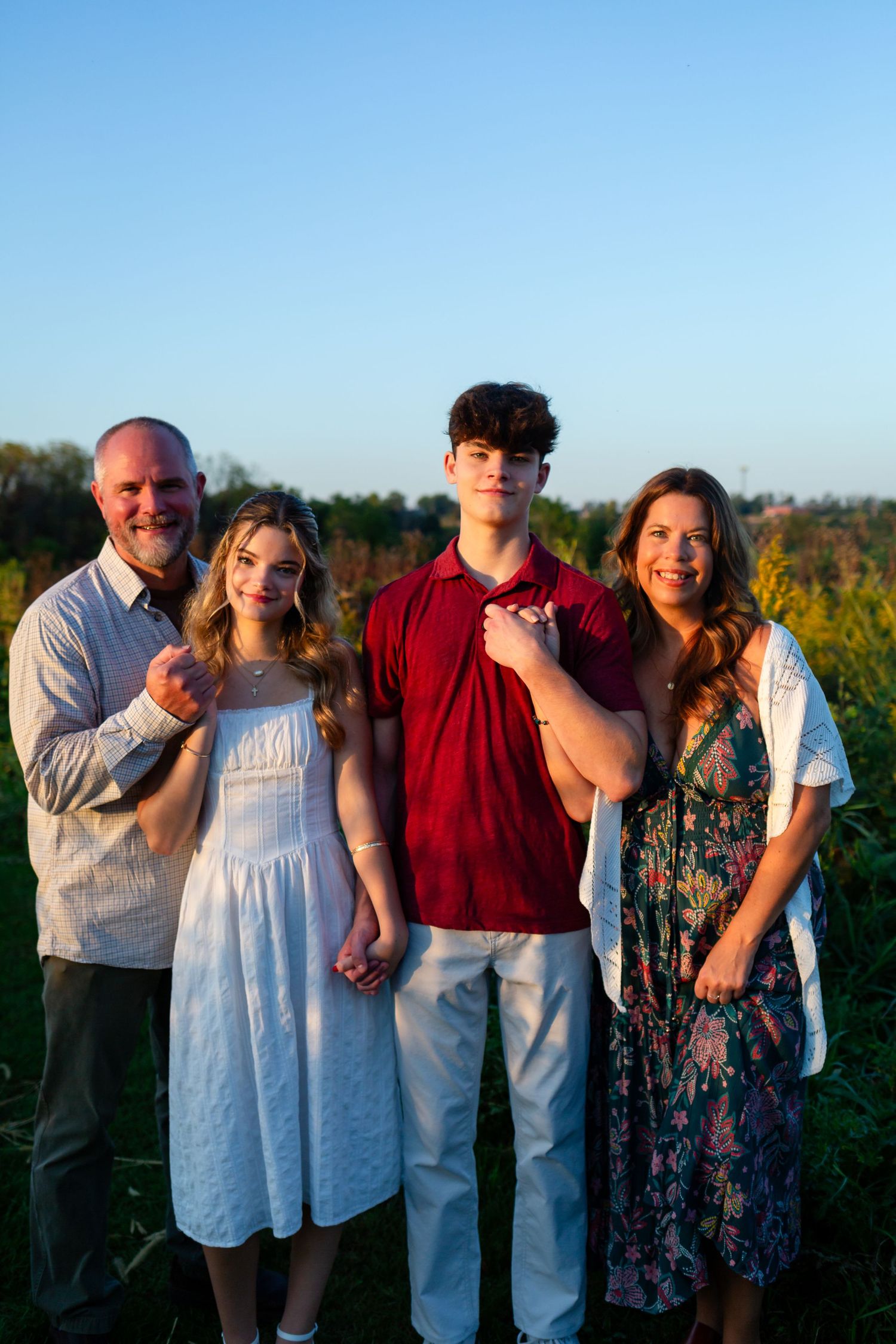 A family group poses together outdoors at Wanatee Park in Marion Iowa during golden hour with trees and natural scenery in the background.