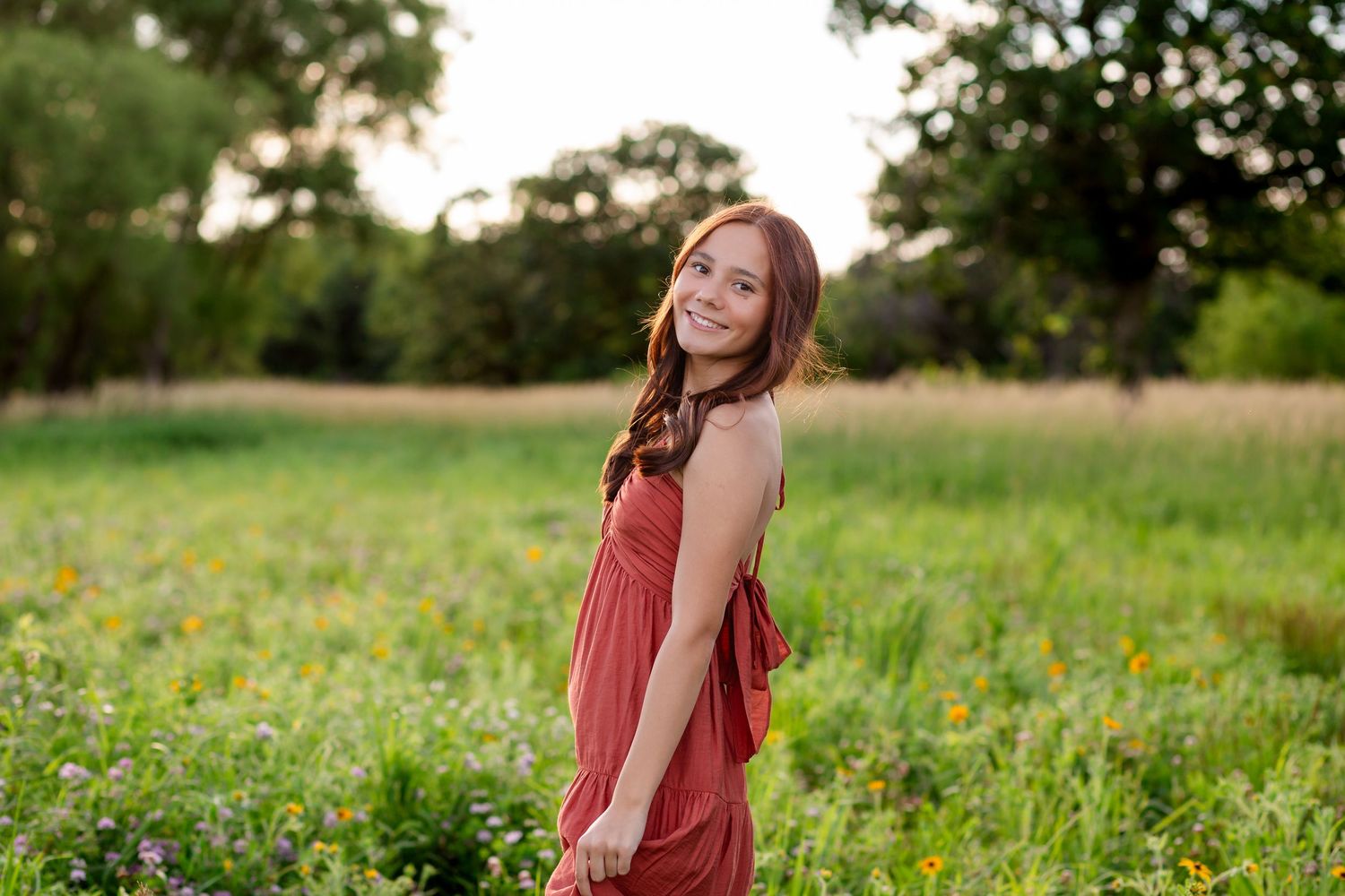 Young woman in red dress smiling in wildflower meadow at golden hour.