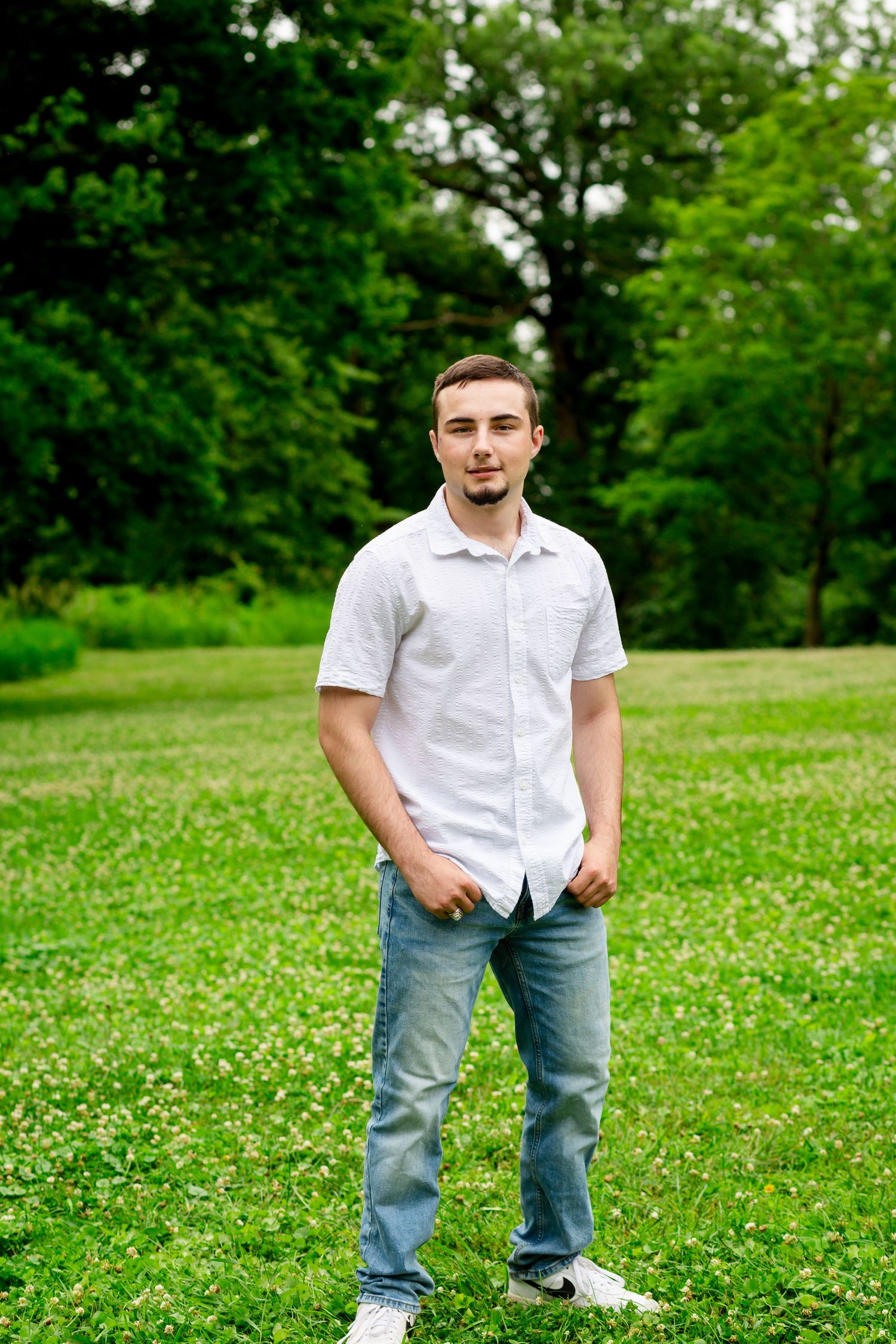 Young man in white shirt and jeans standing on green grass in a park.