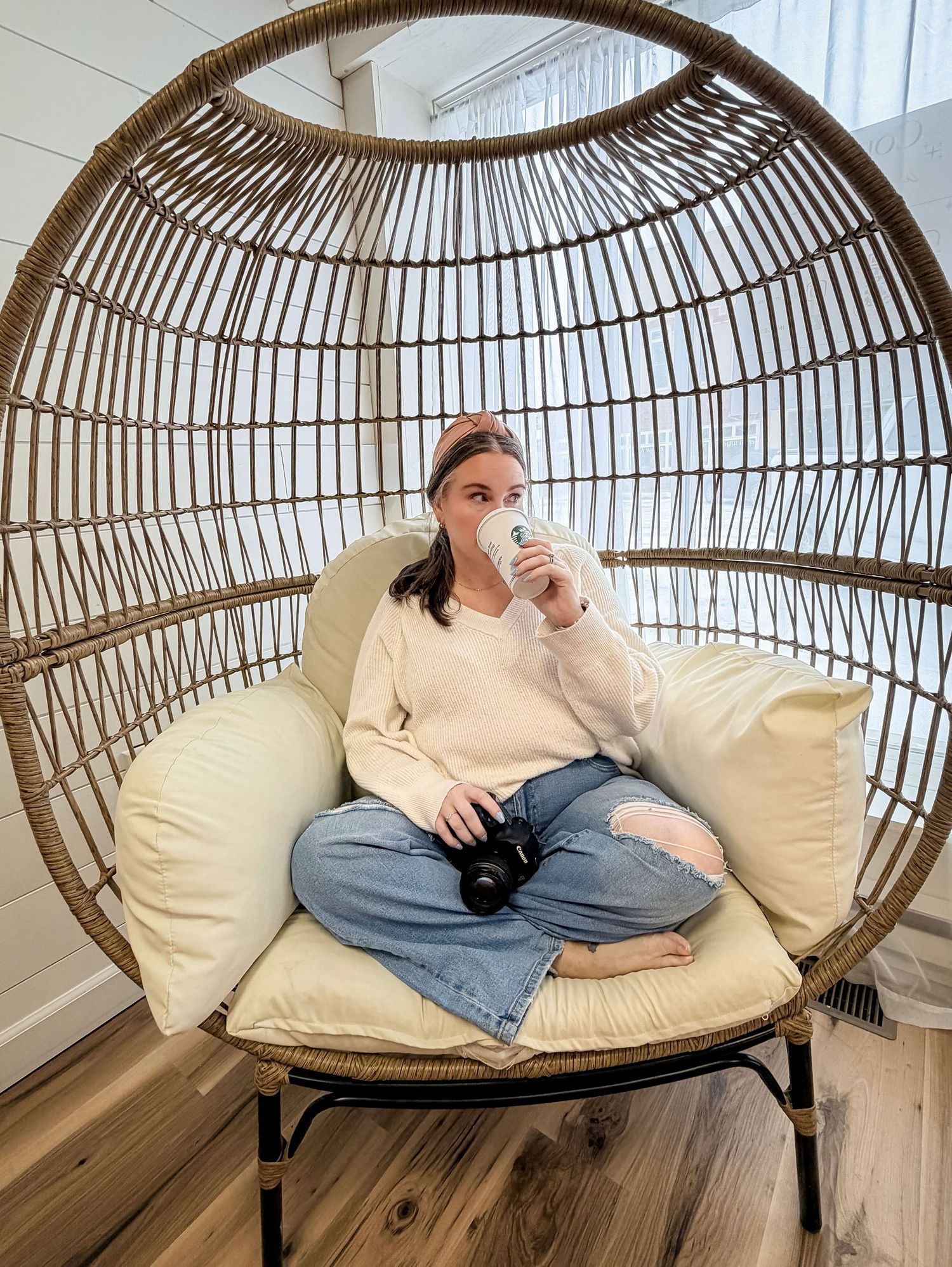 A sequence showing someone lounging comfortably in a modern rattan hanging egg chair with cream cushions.