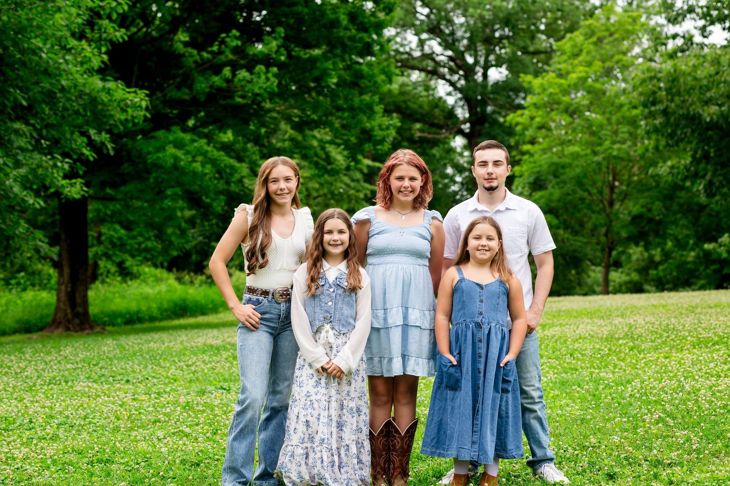 Family of five smiling together outdoors on a lush green lawn.