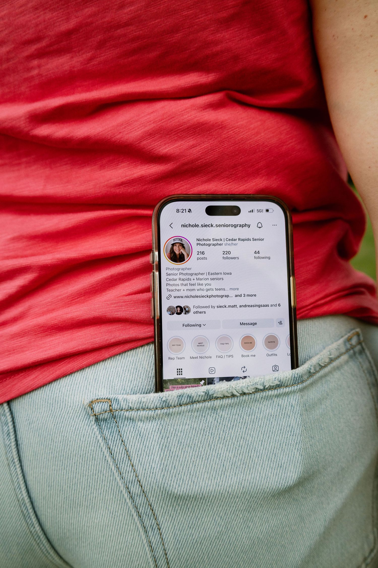 Smartphone displaying an Instagram profile  of a Marion photographer tucked in the back pocket of light blue jeans, and pink shirt
