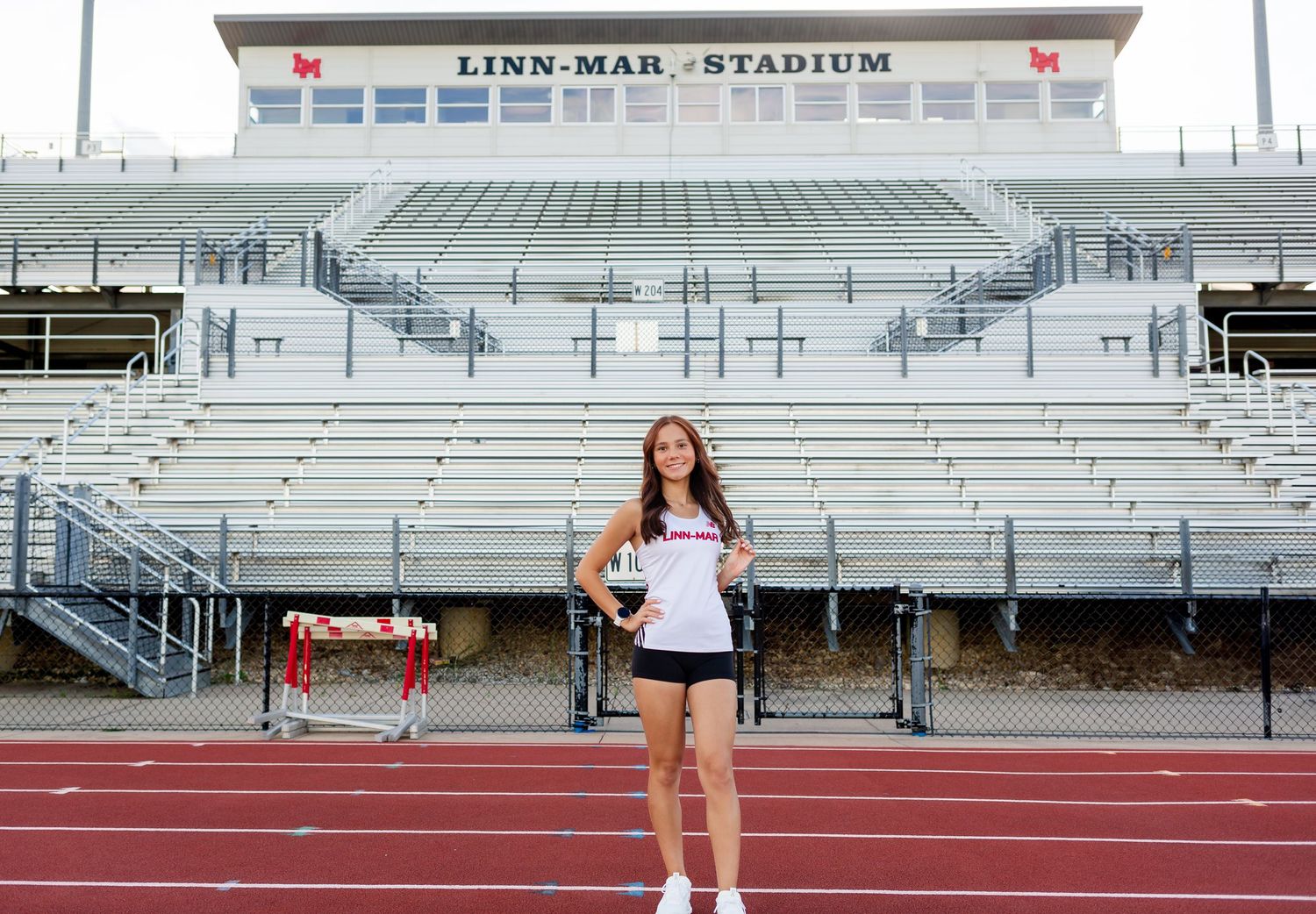 Female athlete poses at Linn-Mar Stadium track, holding an award in athletic wear.