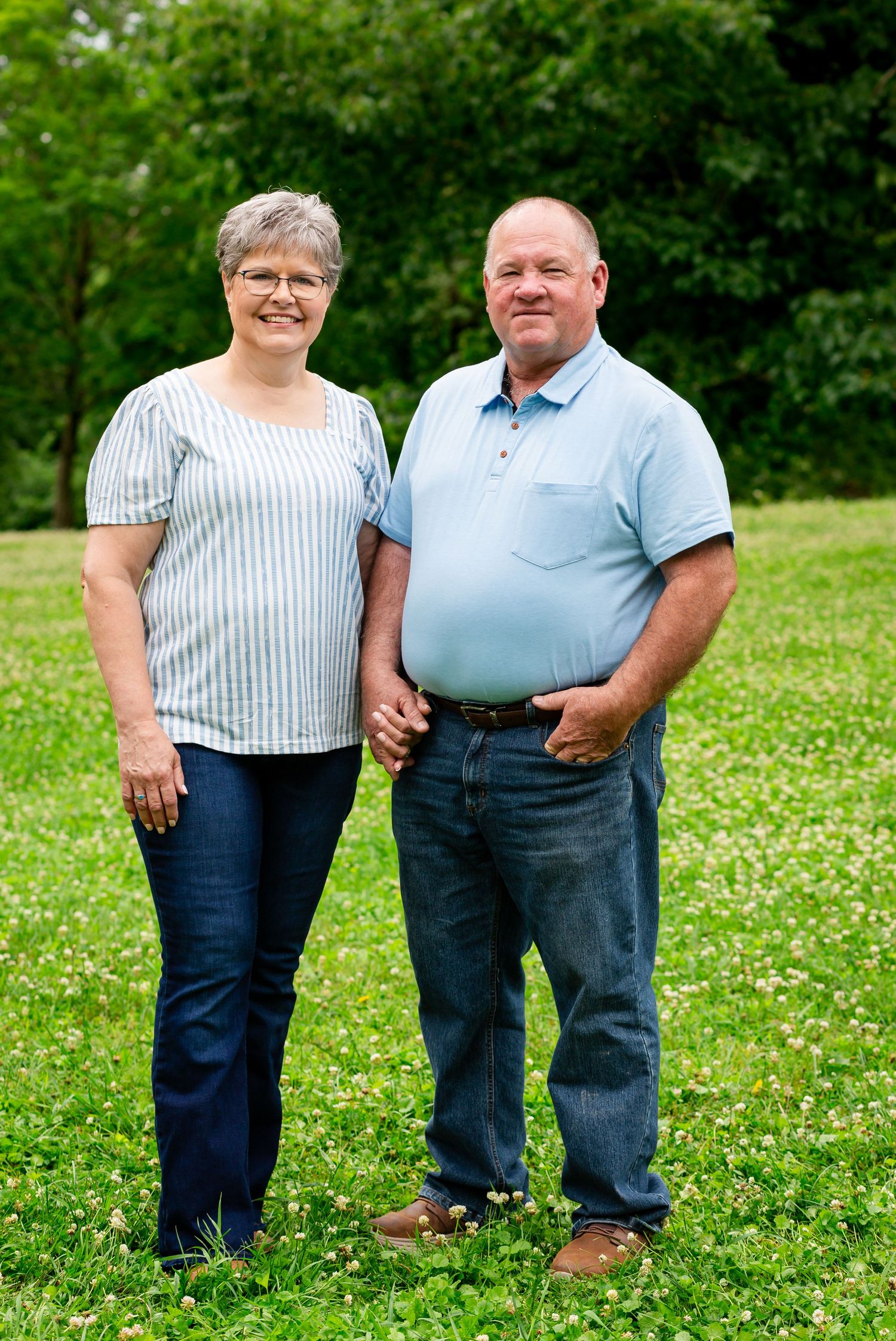 Older couple holding hands and smiling while standing together on a green grassy lawn.