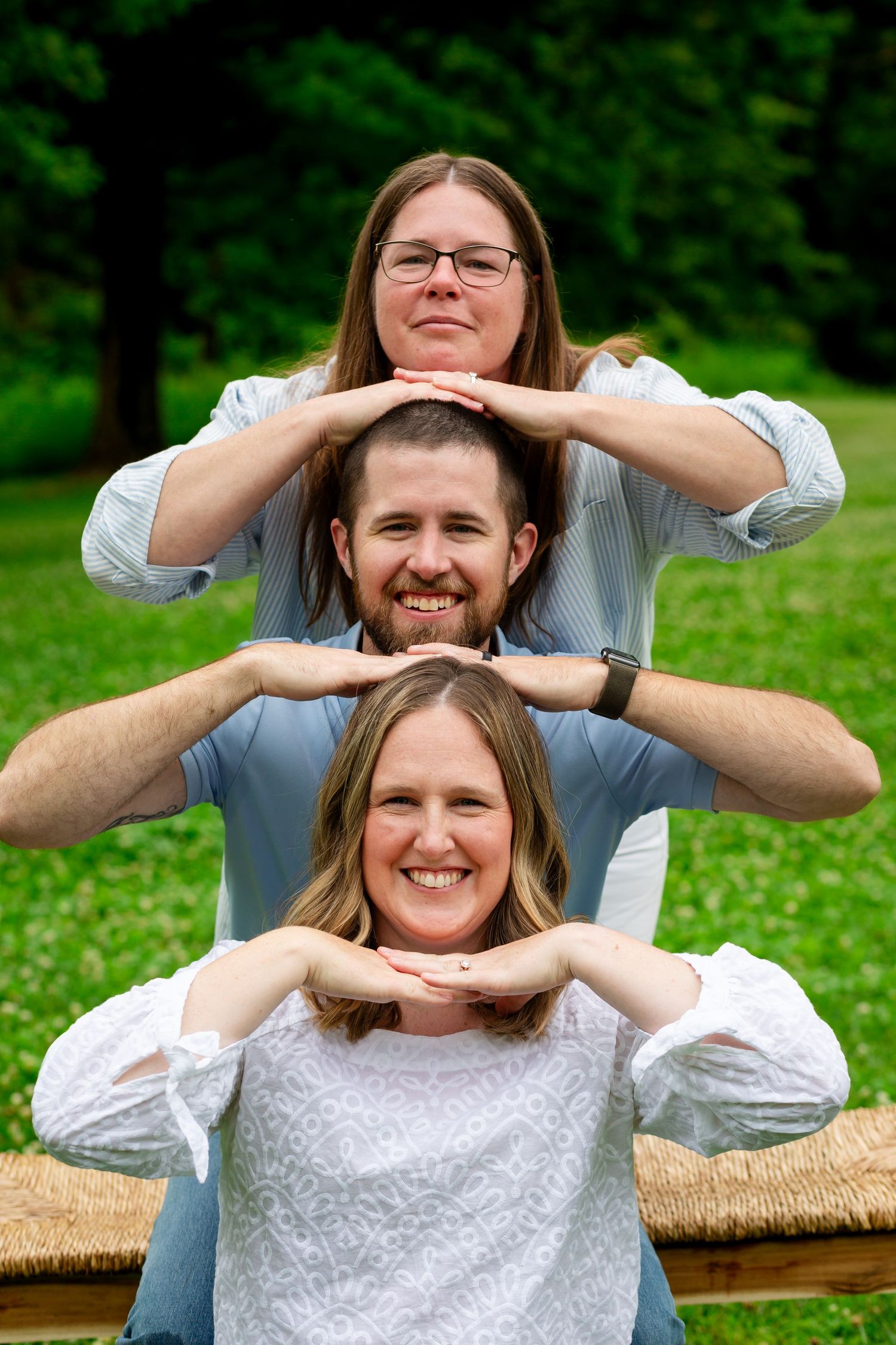 Three people stacking heads in a fun pyramid pose outdoors.