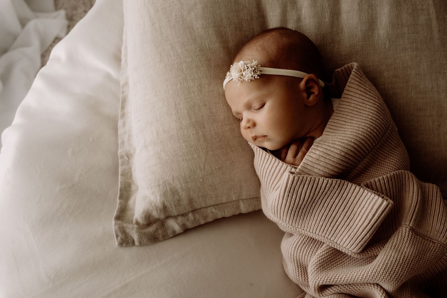 Newborn baby sleeps peacefully wrapped in cozy knit blanket on neutral bedding.