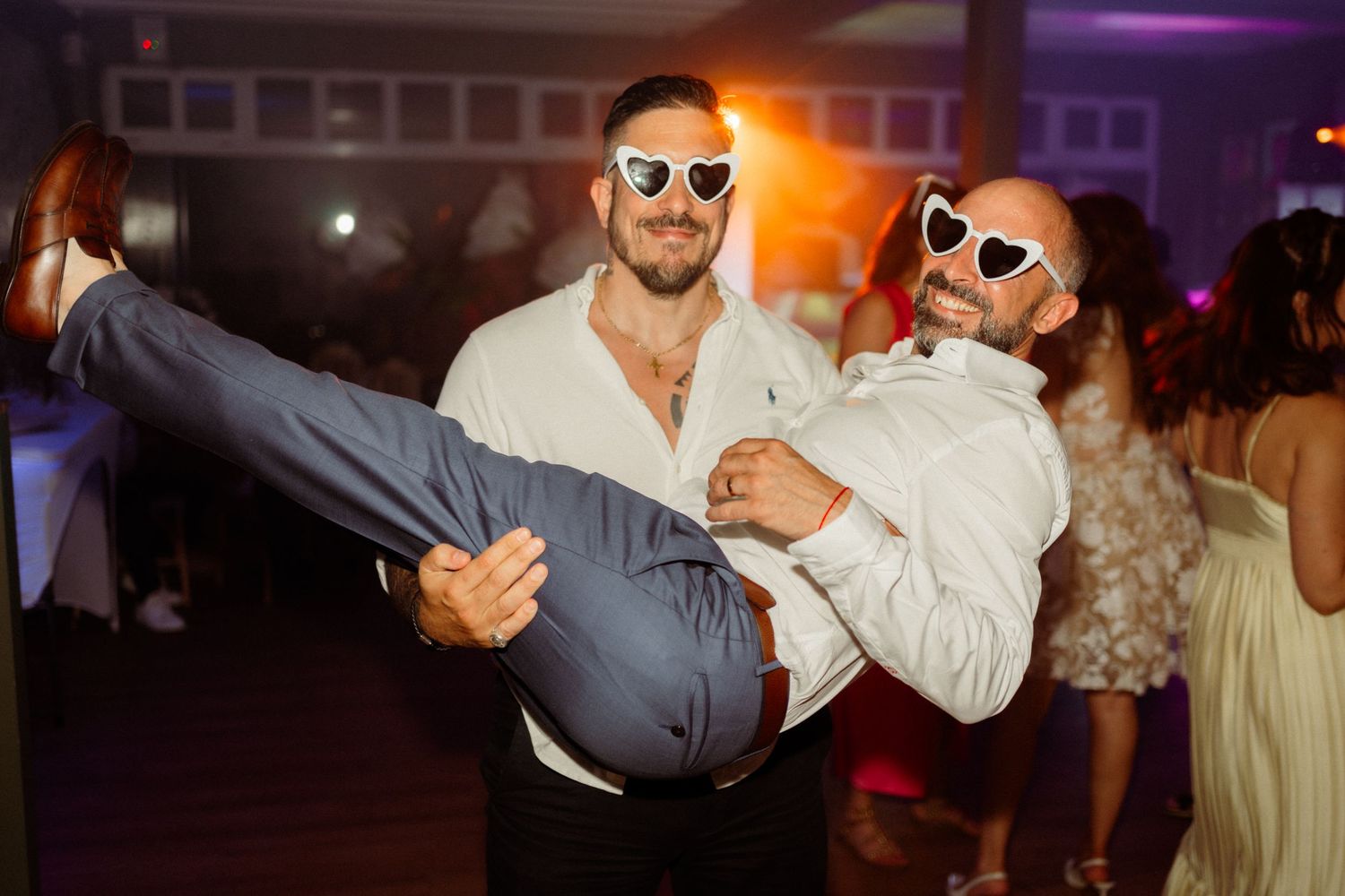 People dance and celebrate at a lively wedding reception with colorful lighting and festive atmosphere.