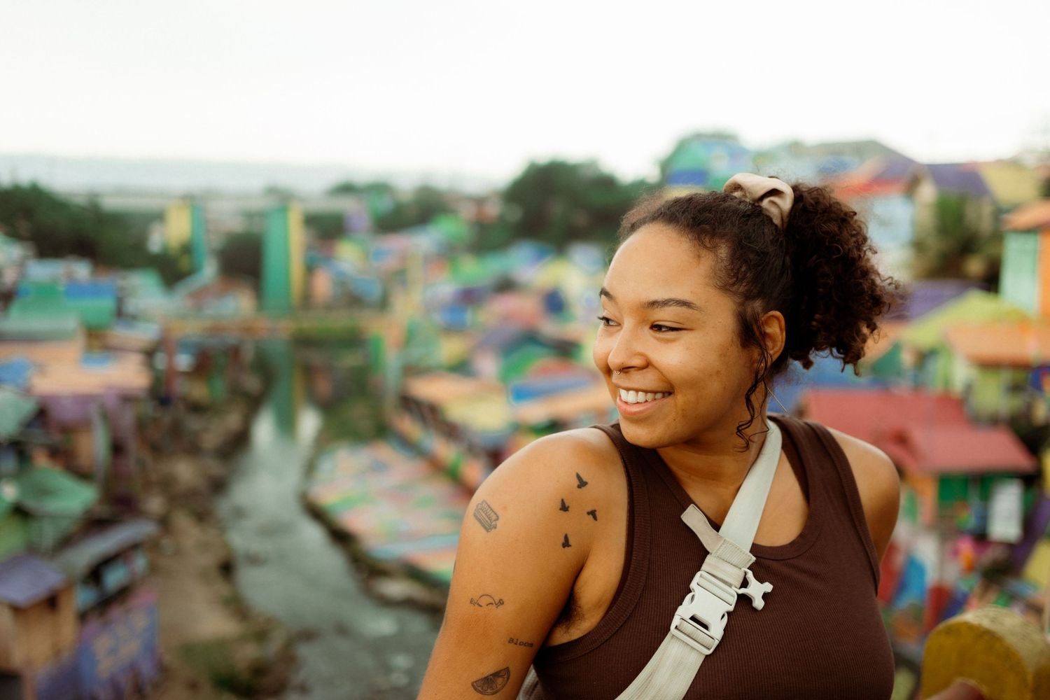 Smiling young woman with tattoos enjoying colorful Kampung Warna-Warni village view in Malang, Indonesia.