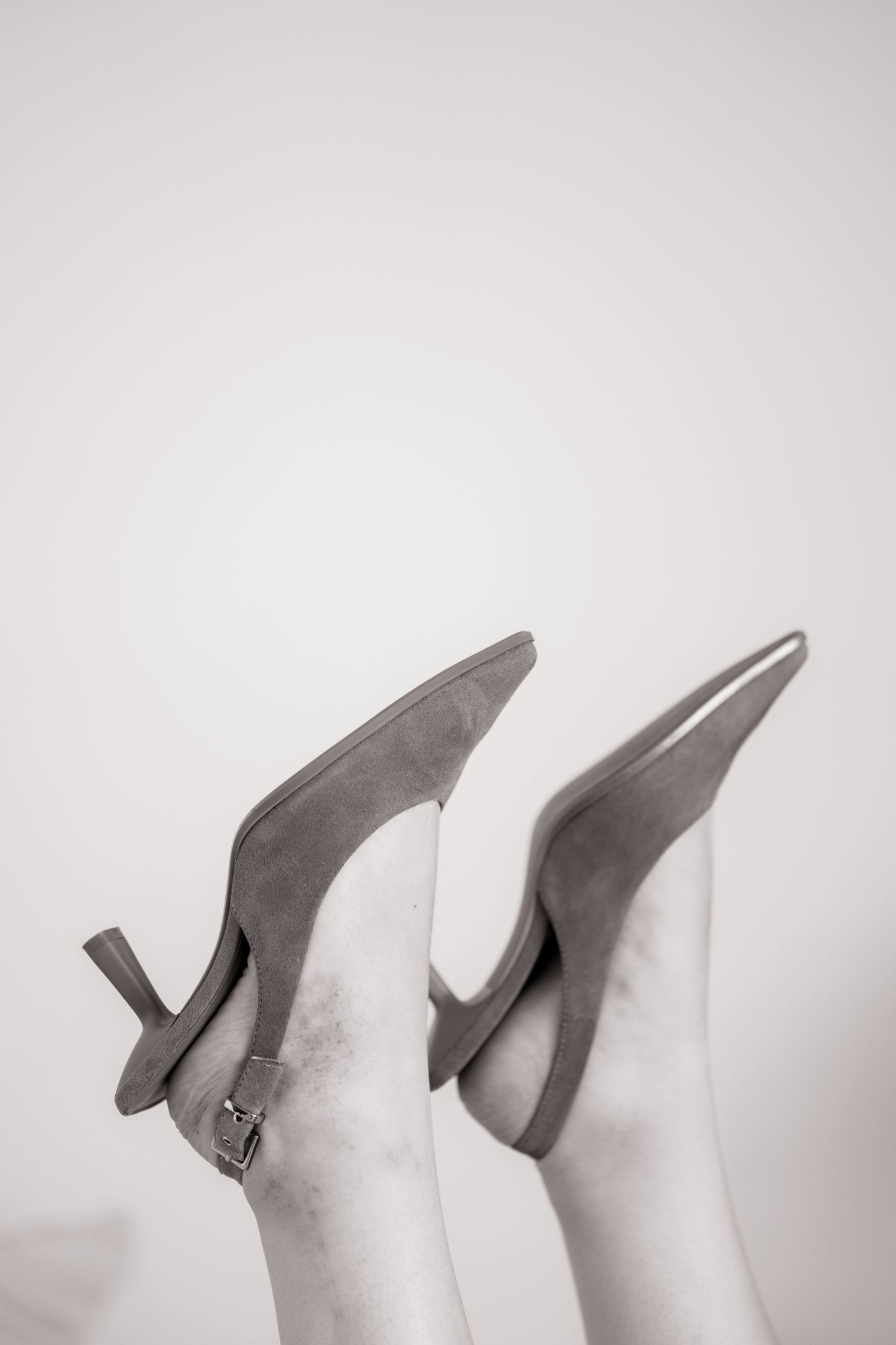 Pair of grey suede high heels shown upside down against white background in black and white photography.