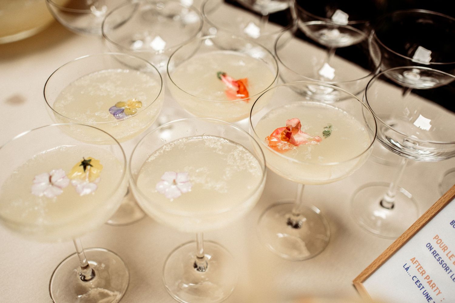 Elegant coupe glasses filled with white cocktails garnished with colorful edible flowers arranged on a table.