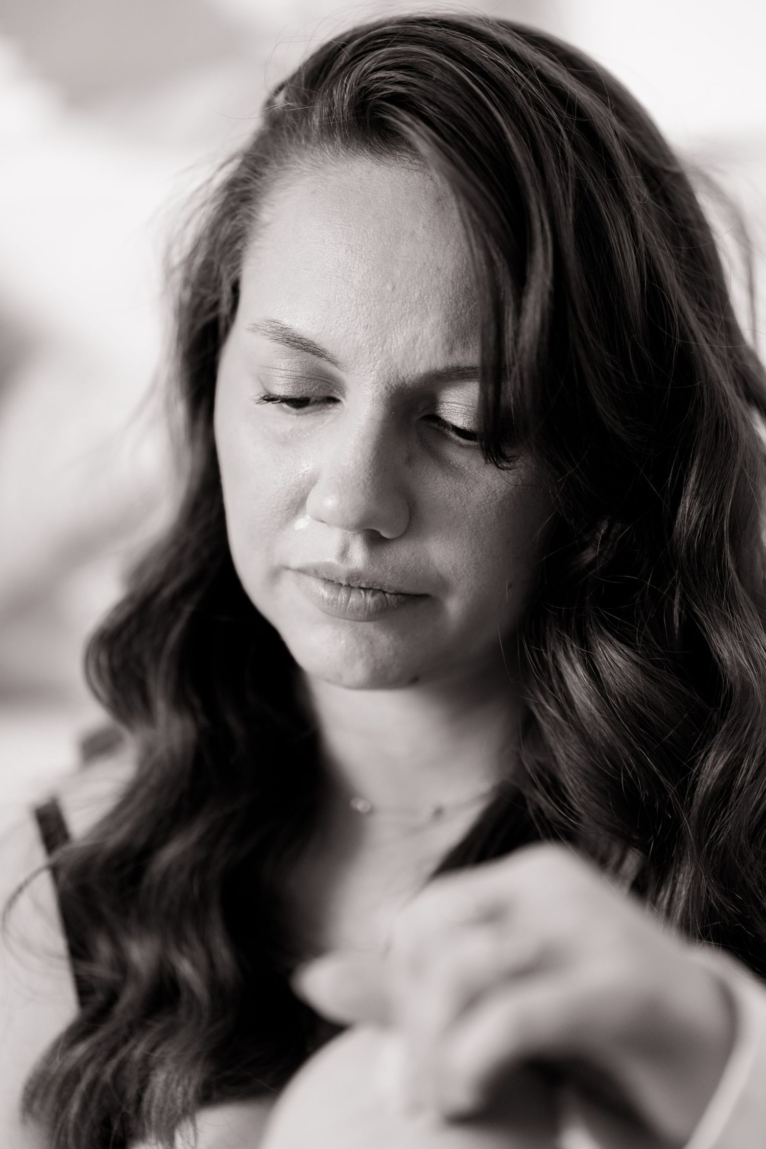 Artistic black and white portrait of a serene woman with long wavy dark hair looking down.