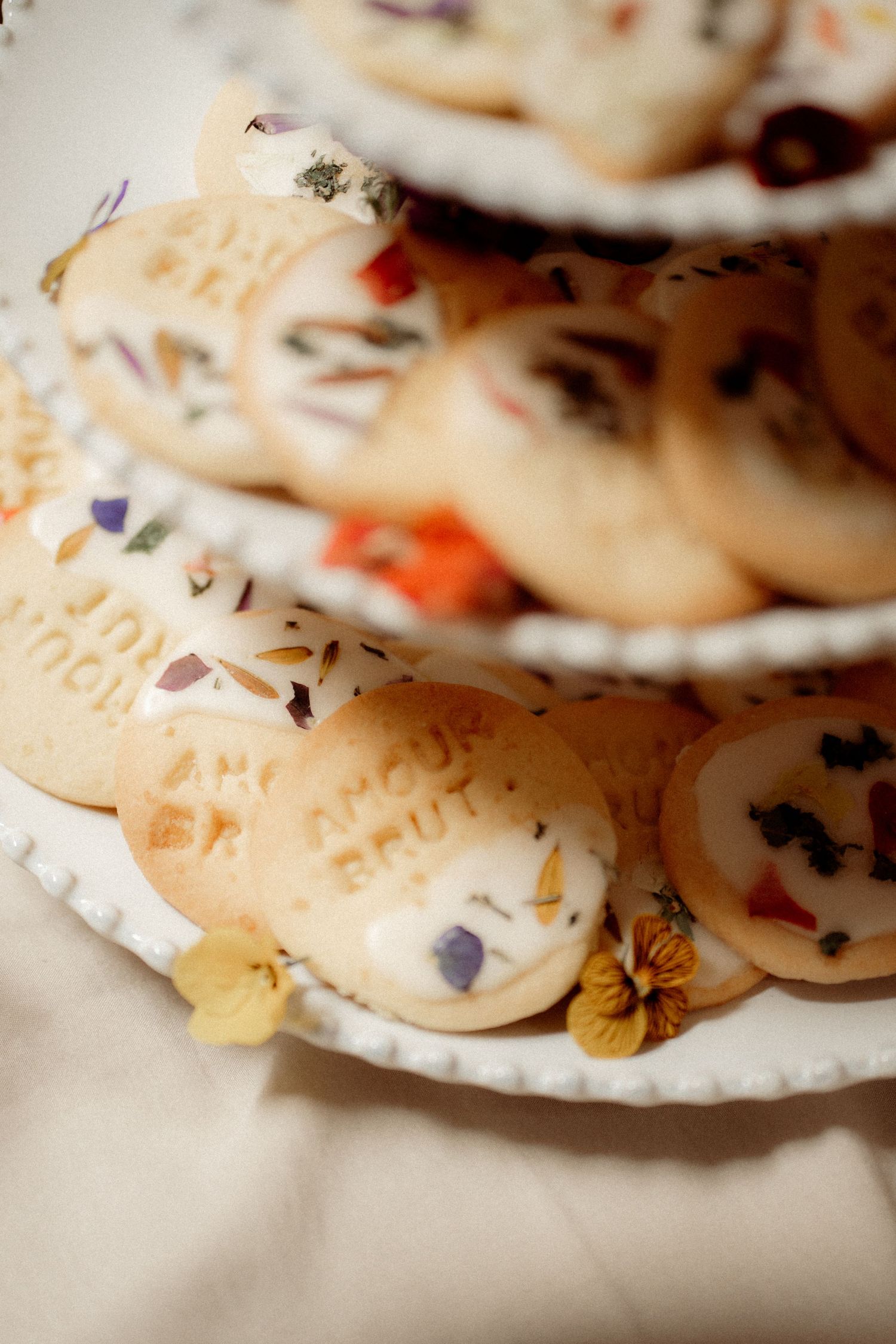 Tiered display of round wedding cookies with floral decorations and stamped text on white platters.